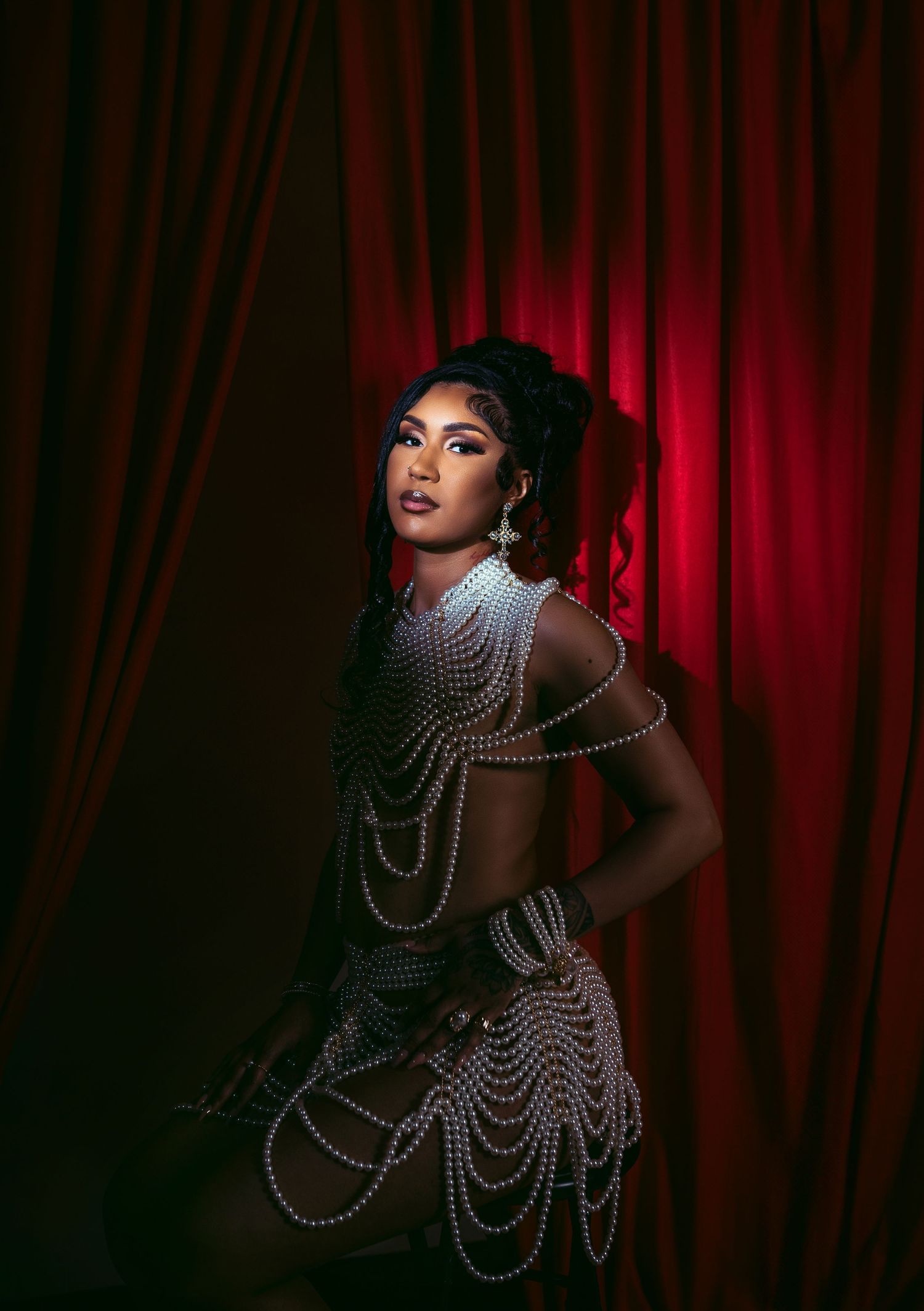 Dramatic portrait of model in pearl-draped dress against red velvet curtain.