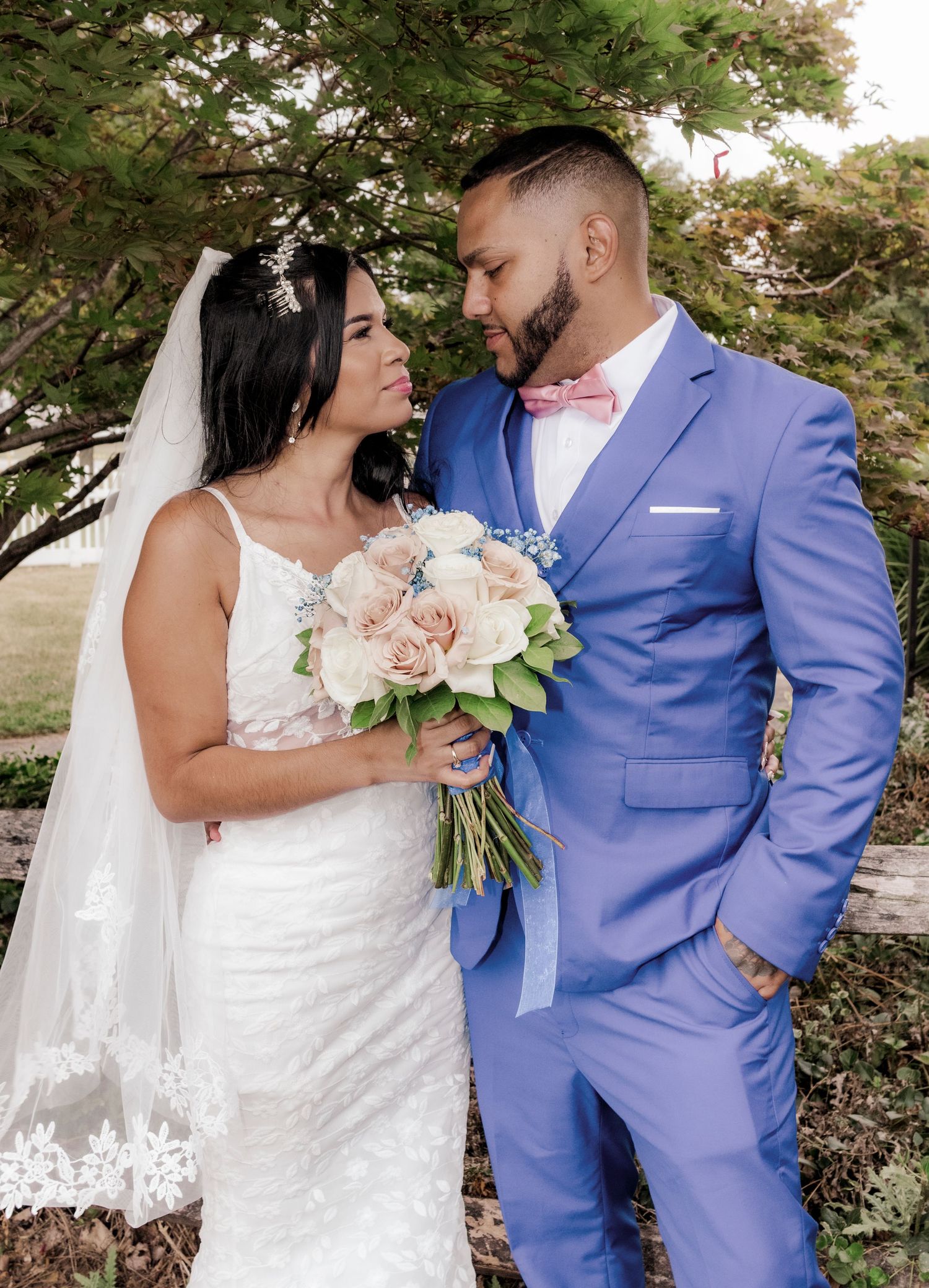 Beautiful wedding couple in a lace dress and light blue suit sharing an intimate moment with pink bouquet.