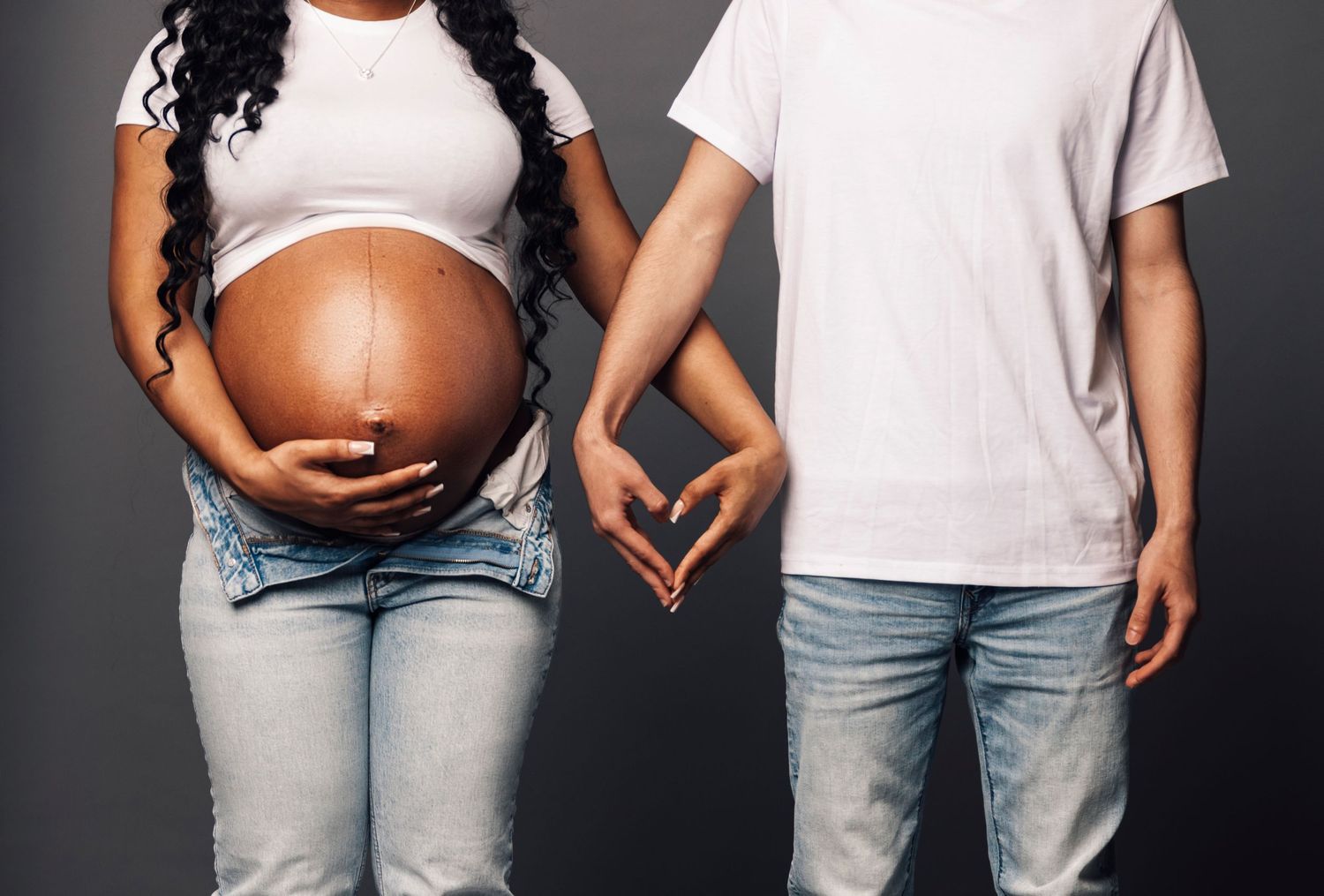 A minimalist maternity photo showing couple making heart shape with hands over baby bump.
