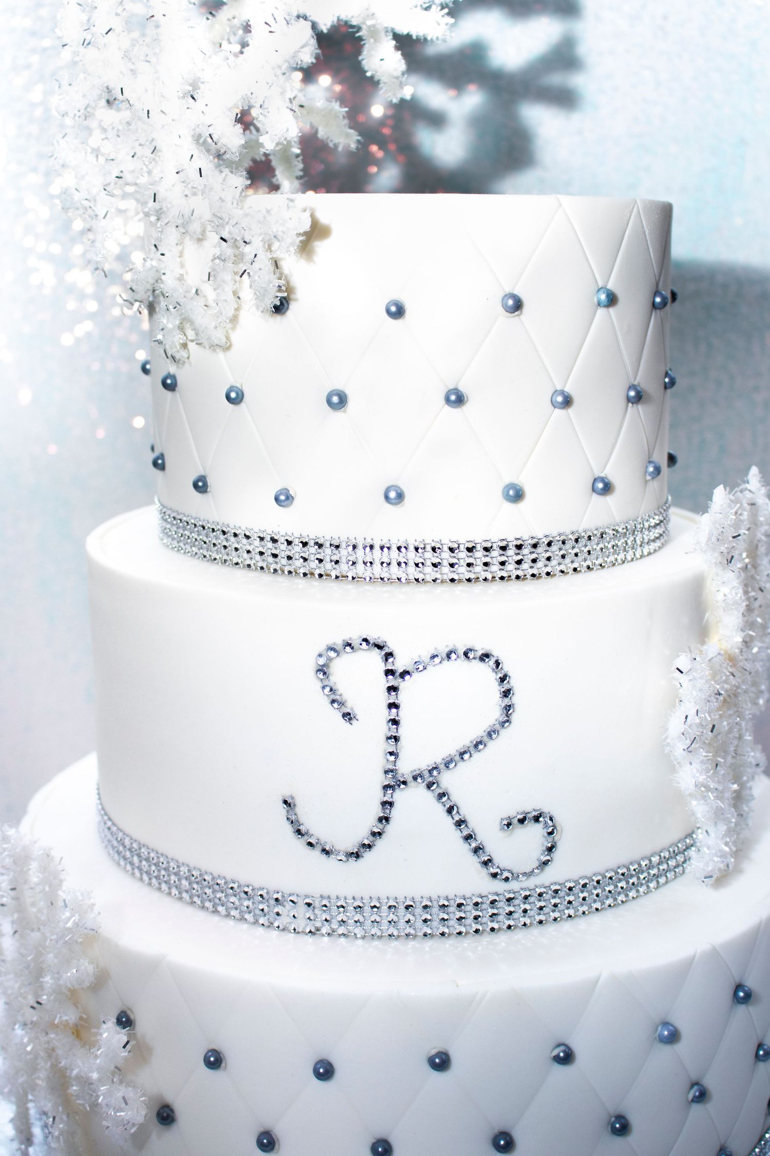 Close-up details of an elegant white wedding cake decorated with navy blue pearls and crystal rhinestone trim.