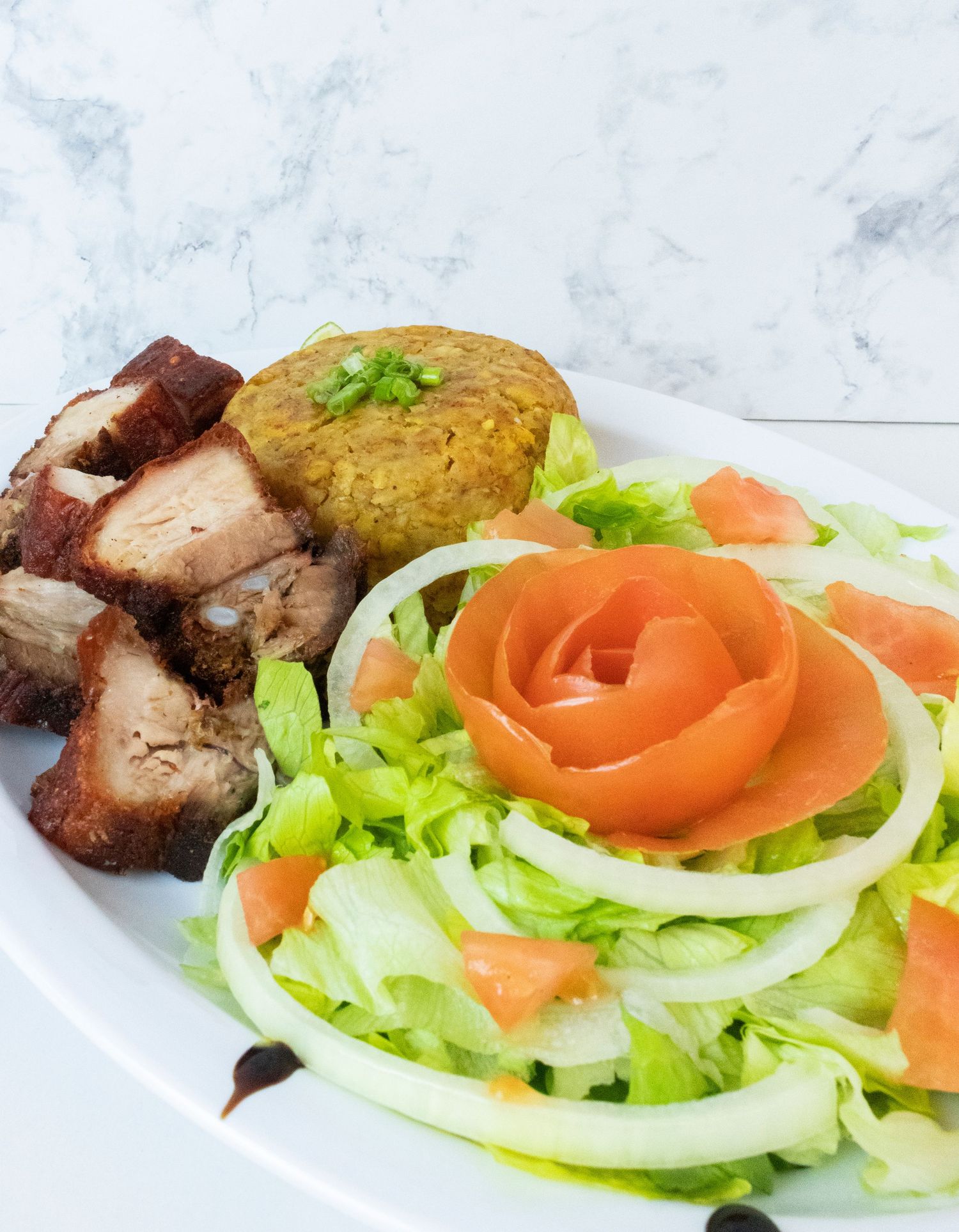 Grilled meat with rice patty served alongside fresh salad with tomato rose garnish on white plate.