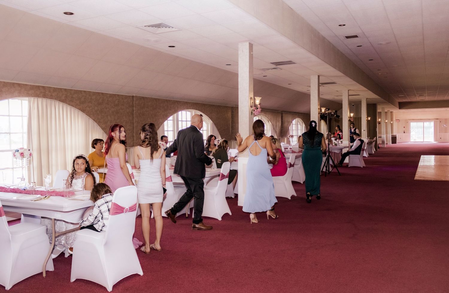 Wedding reception venue with tables and guests in pink and white decor.