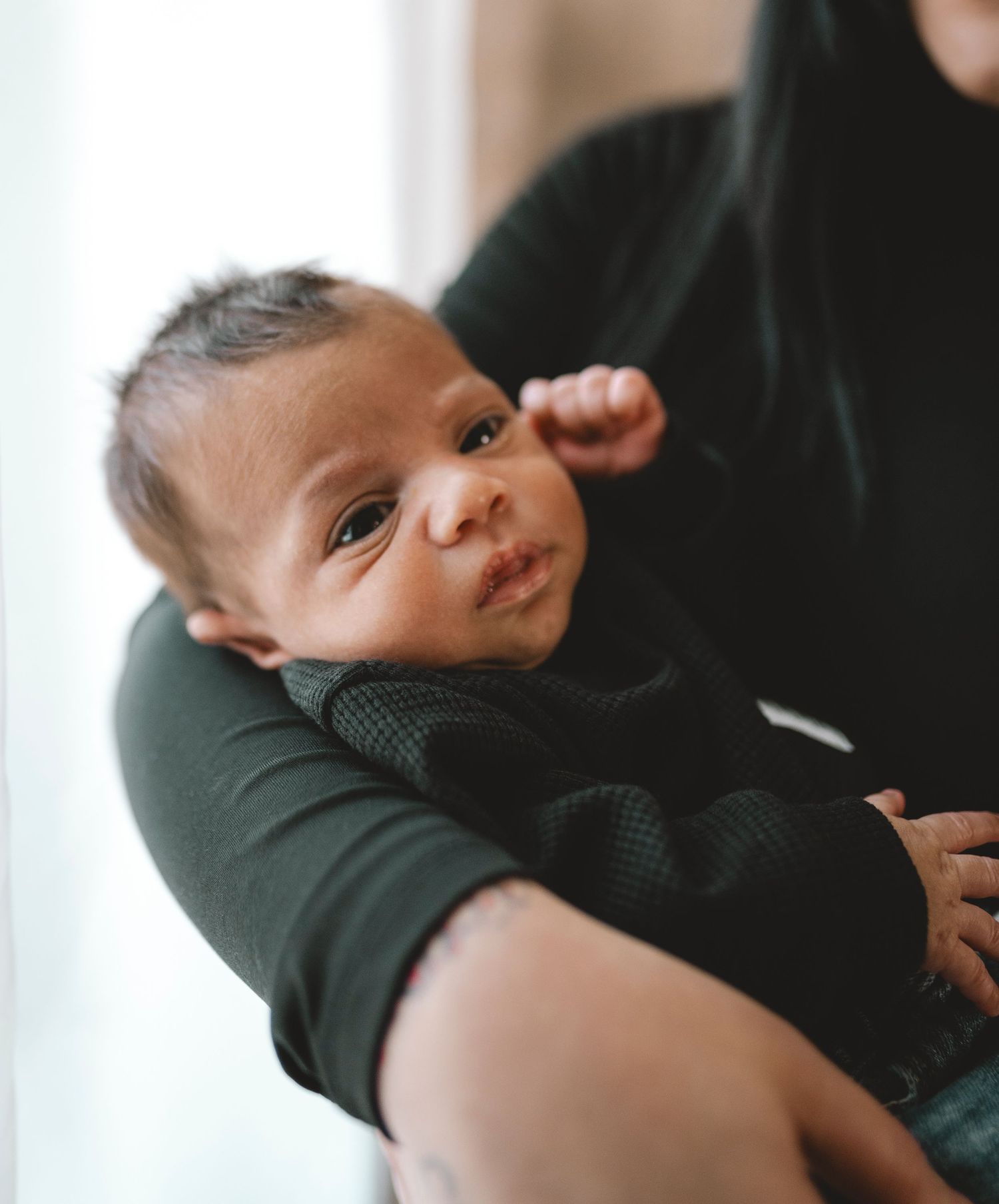 A newborn baby with dark hair being cradled in the arms of a person wearing a dark green outfit.