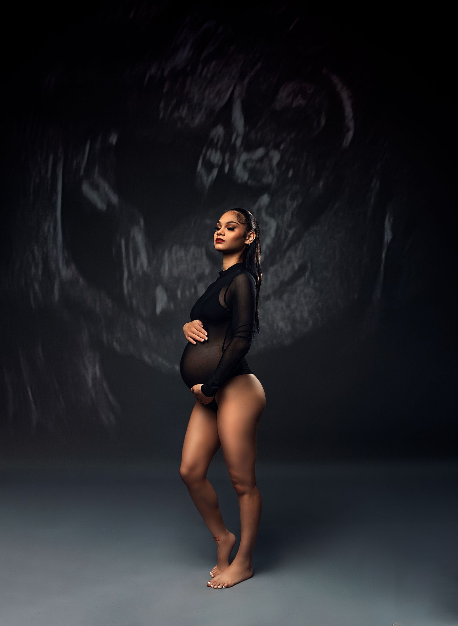 Maternity portrait with dramatic lighting showing expectant mother in black bodysuit.