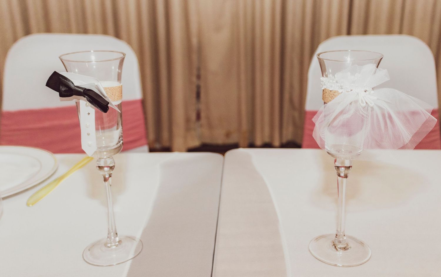 Two champagne flutes decorated with black and white bows on wedding reception table.