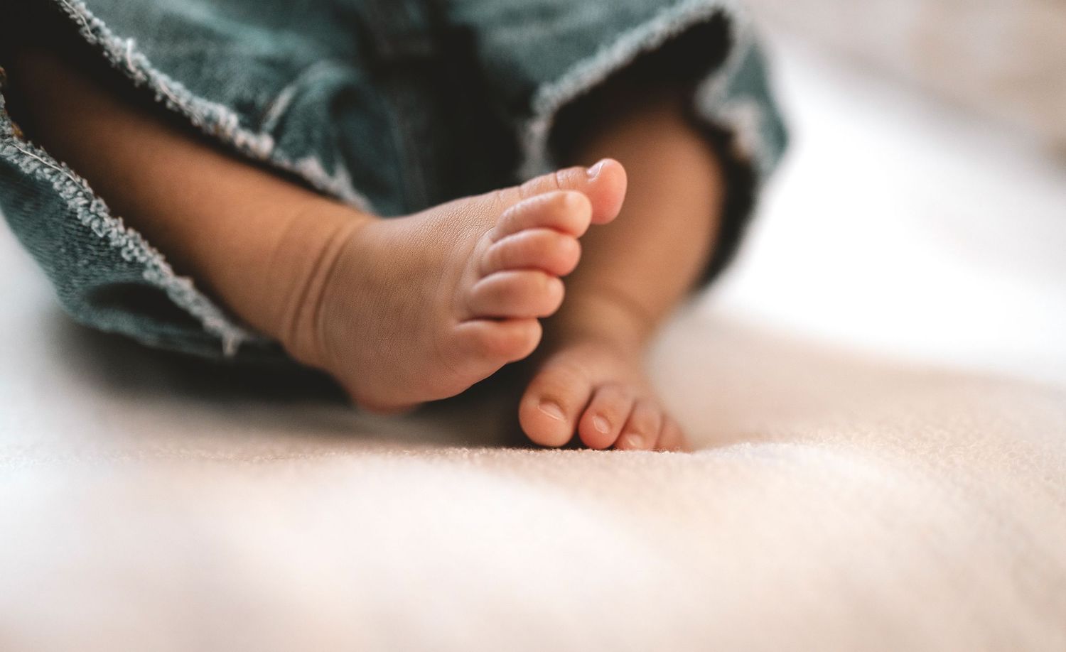 Close-up of cute newborn baby feet resting on a soft white blanket, wearing denim pants.
