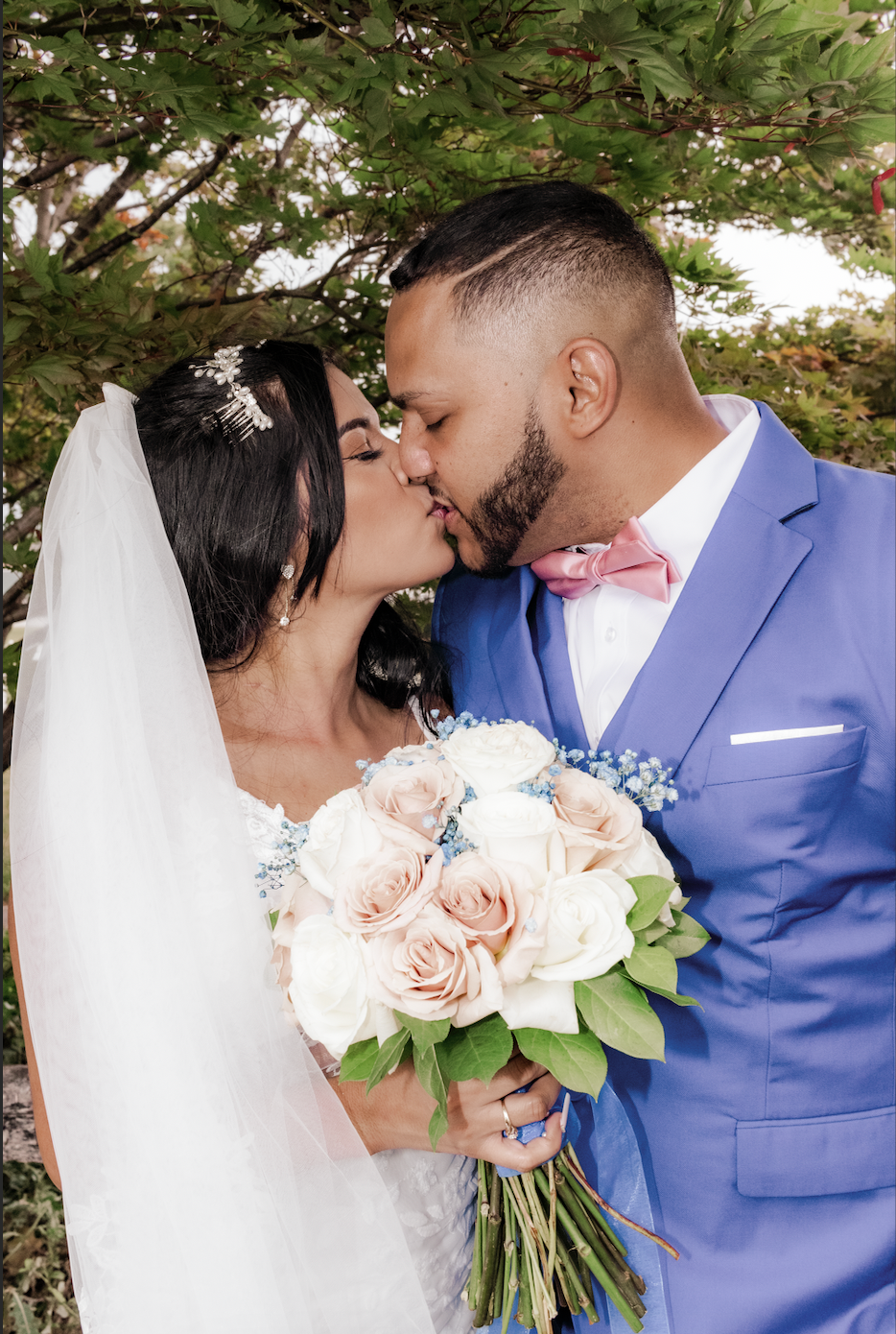 Romantic wedding couple sharing kiss while holding blush rose bouquet.