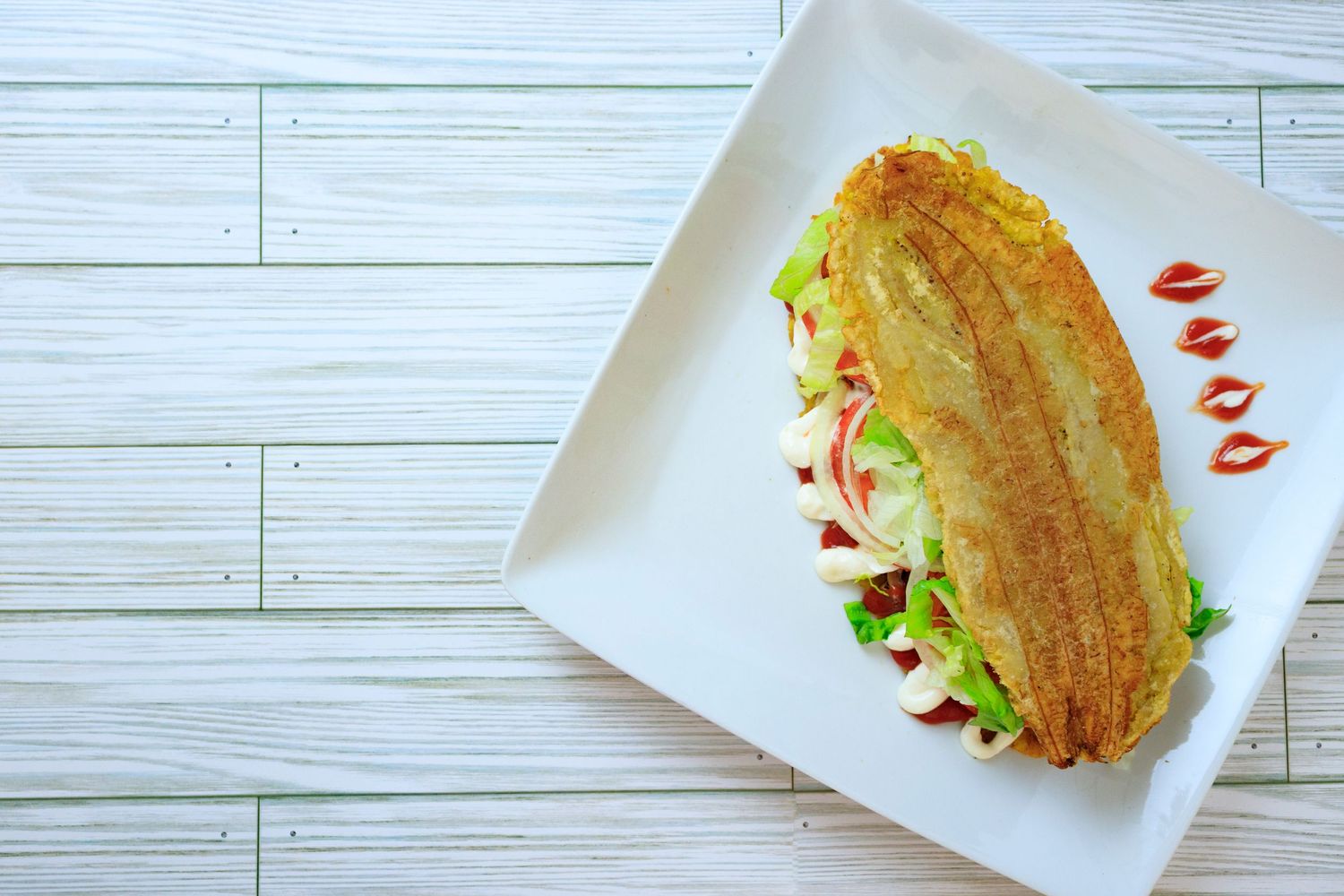 Toasted submarine sandwich with lettuce and sauce on white square plate.