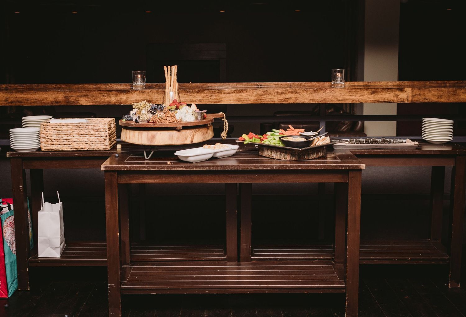 A long wooden bar counter with stacked plates and glassware in a dimly lit rustic restaurant interior.