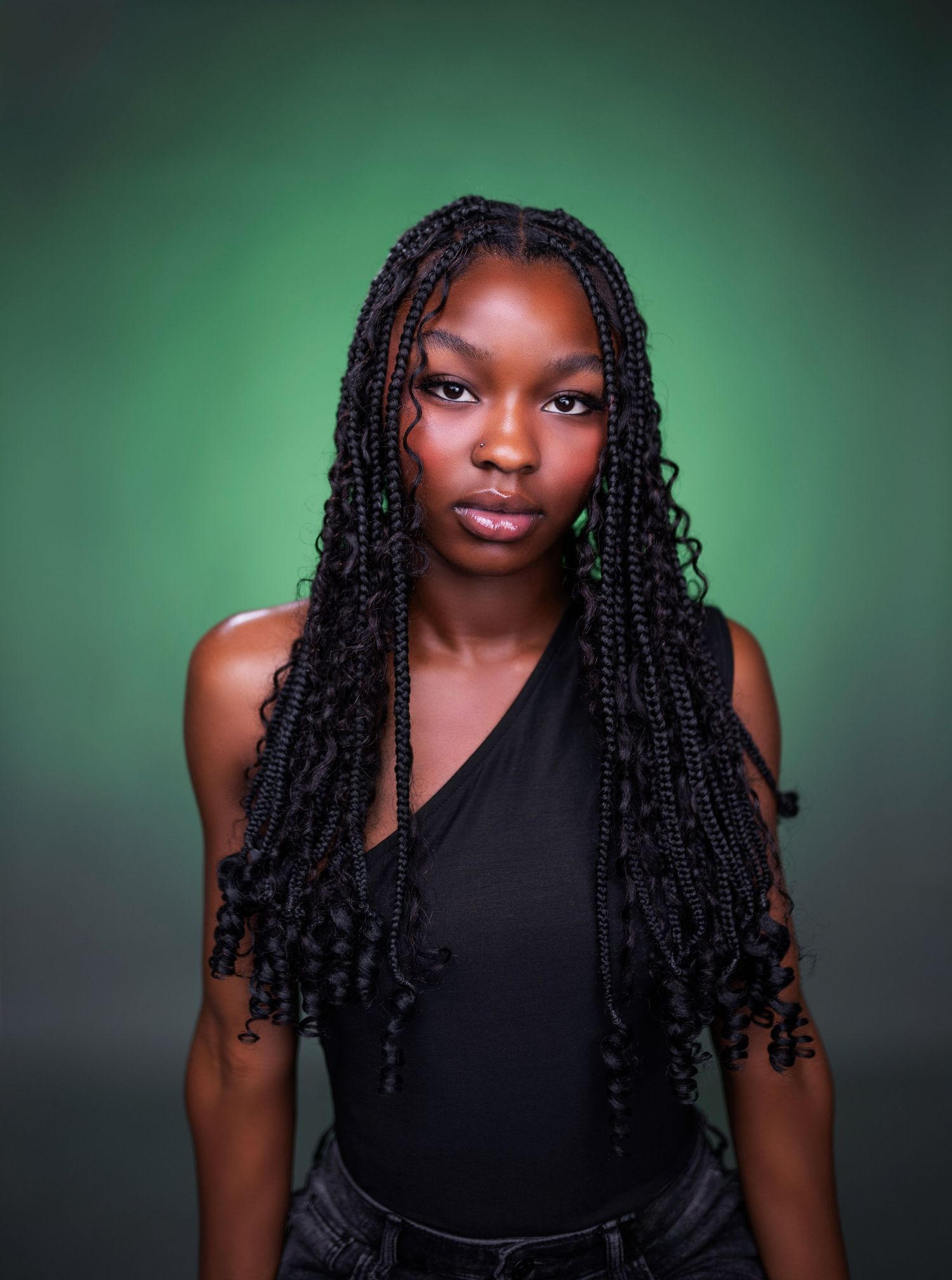 Portrait against green background featuring long braided hair and black top with dramatic studio lighting.