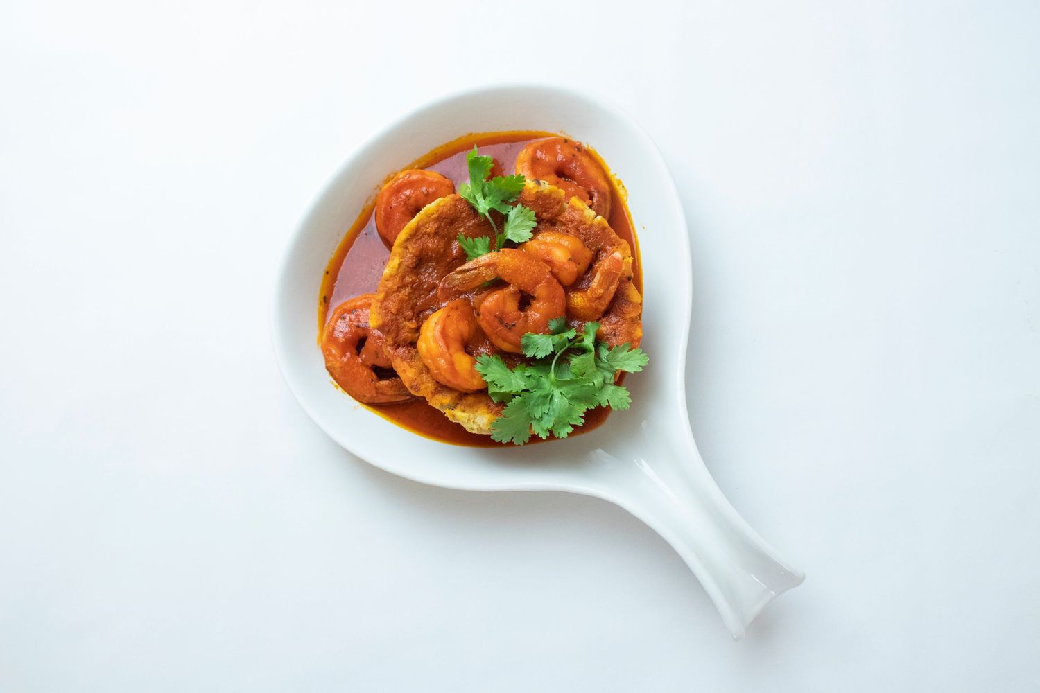 Spicy shrimp curry garnished with cilantro in a white serving spoon.