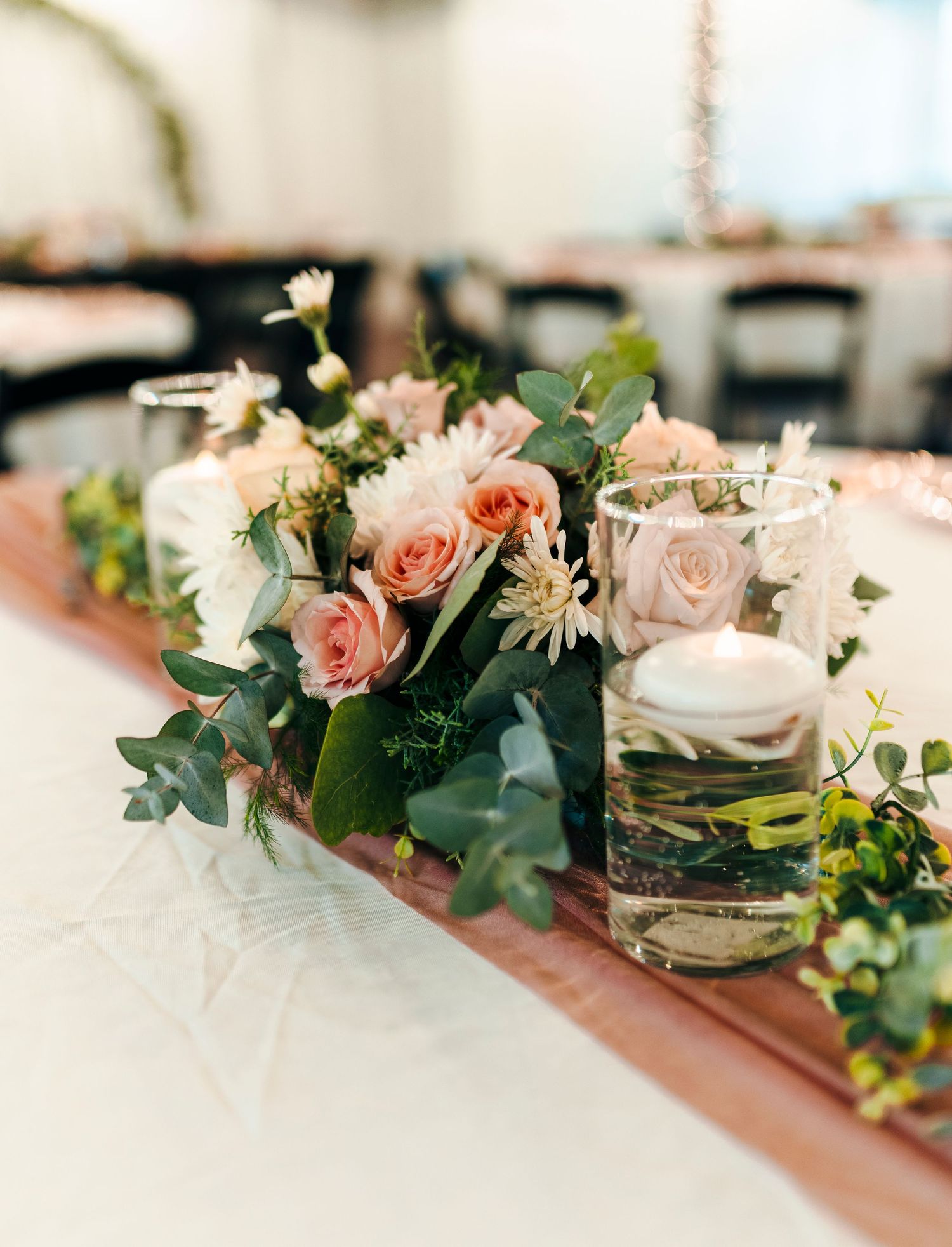 Romantic wedding centerpiece with blush roses, white flowers, eucalyptus, and glass candle holders.