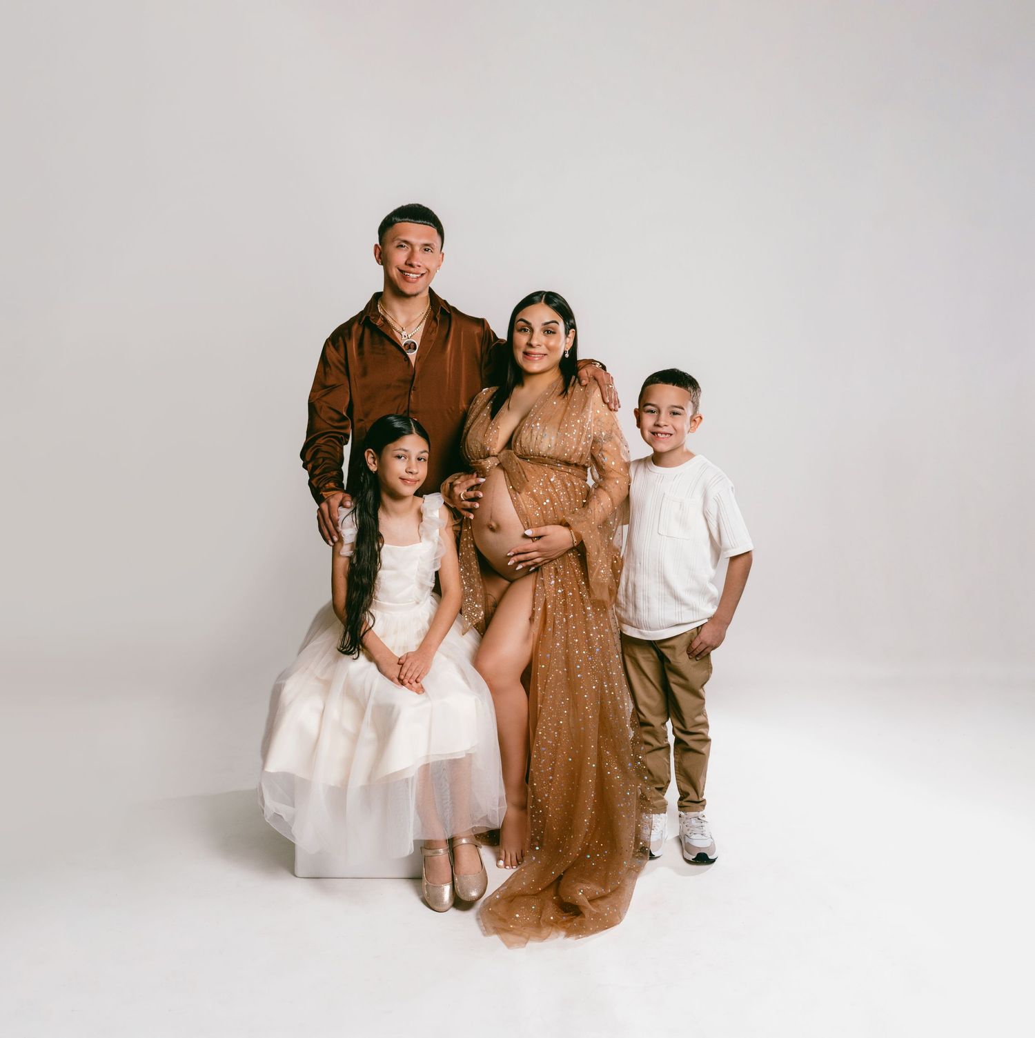 Studio family portrait with expecting parents and two children against white background.