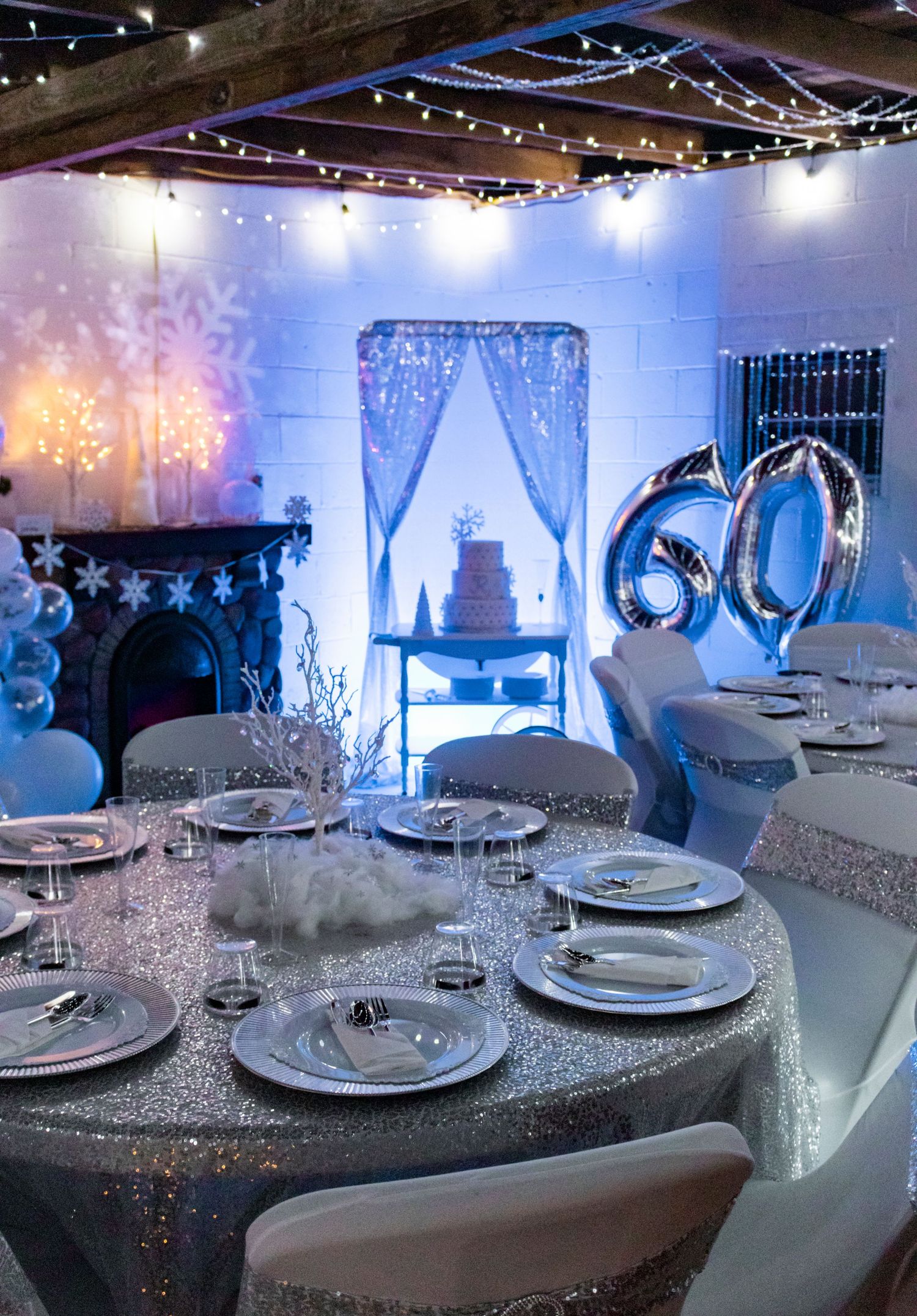 Elegant winter wonderland party setup with silver decor and blue lighting for 60th celebration.