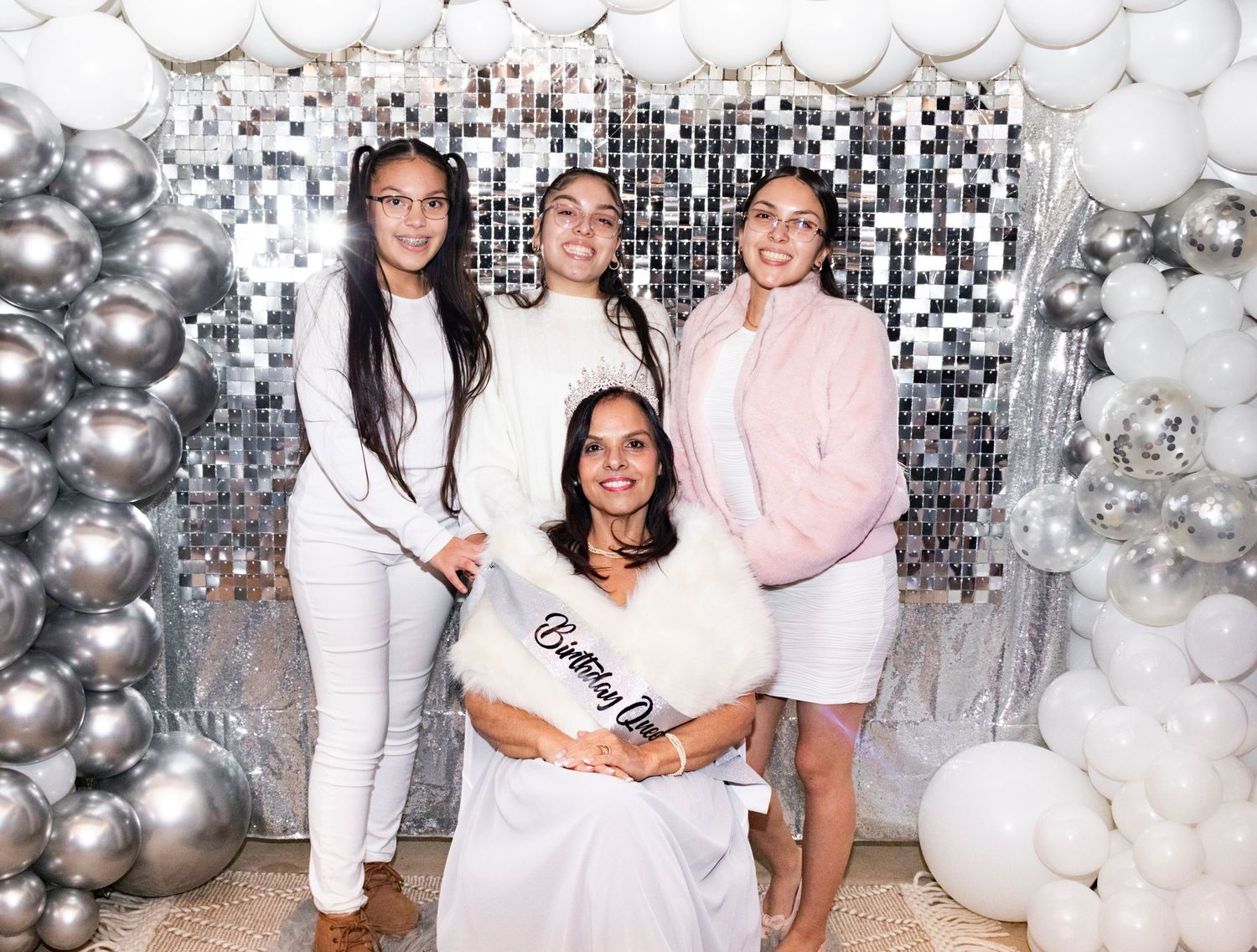 People pose together at a party with white and silver balloon decorations in the background.