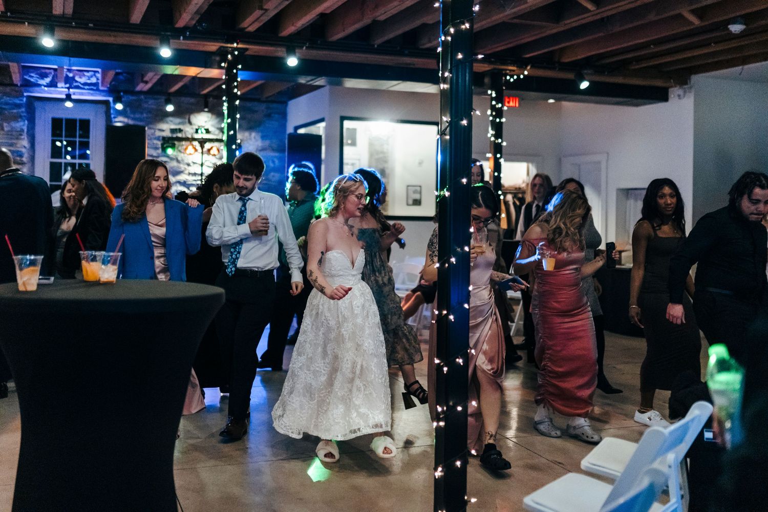 Bride dances with guests on a dimly lit dance floor decorated with fairy lights at wedding reception.