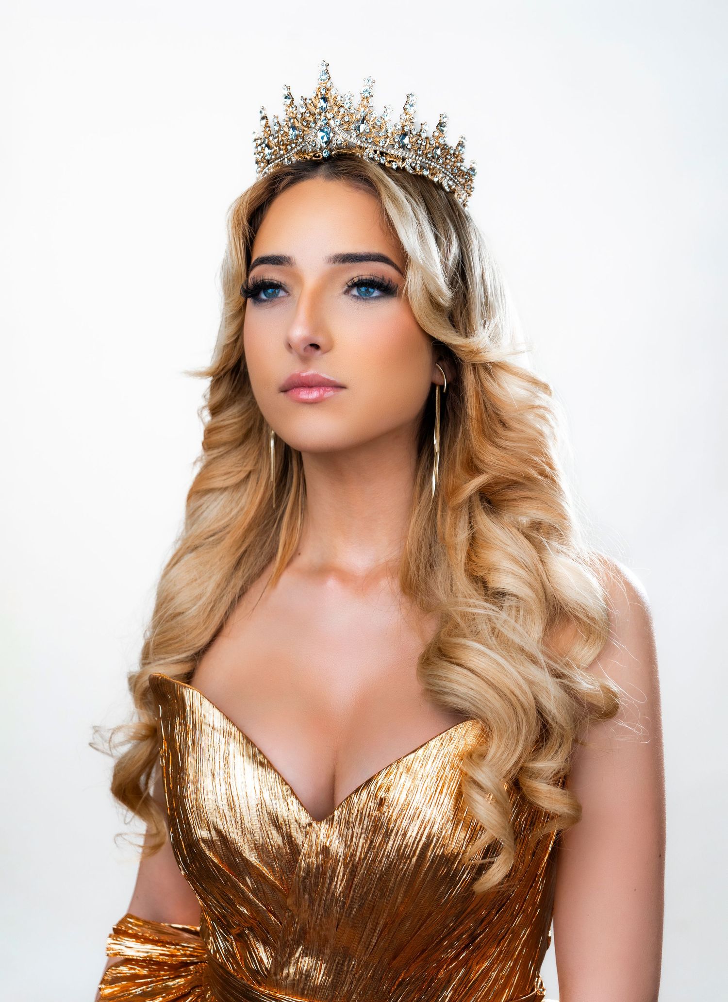 Glamour portrait in gold gown and crystal crown against white background.