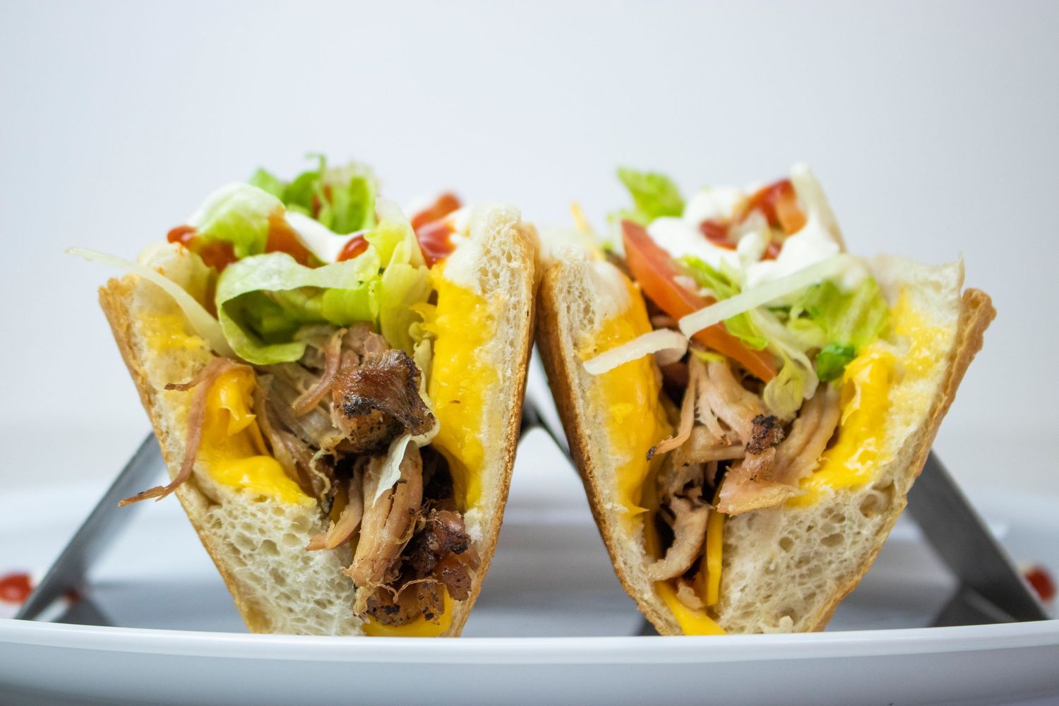 Two loaded tacos with shredded meat, lettuce and cheese served on metal taco holders.