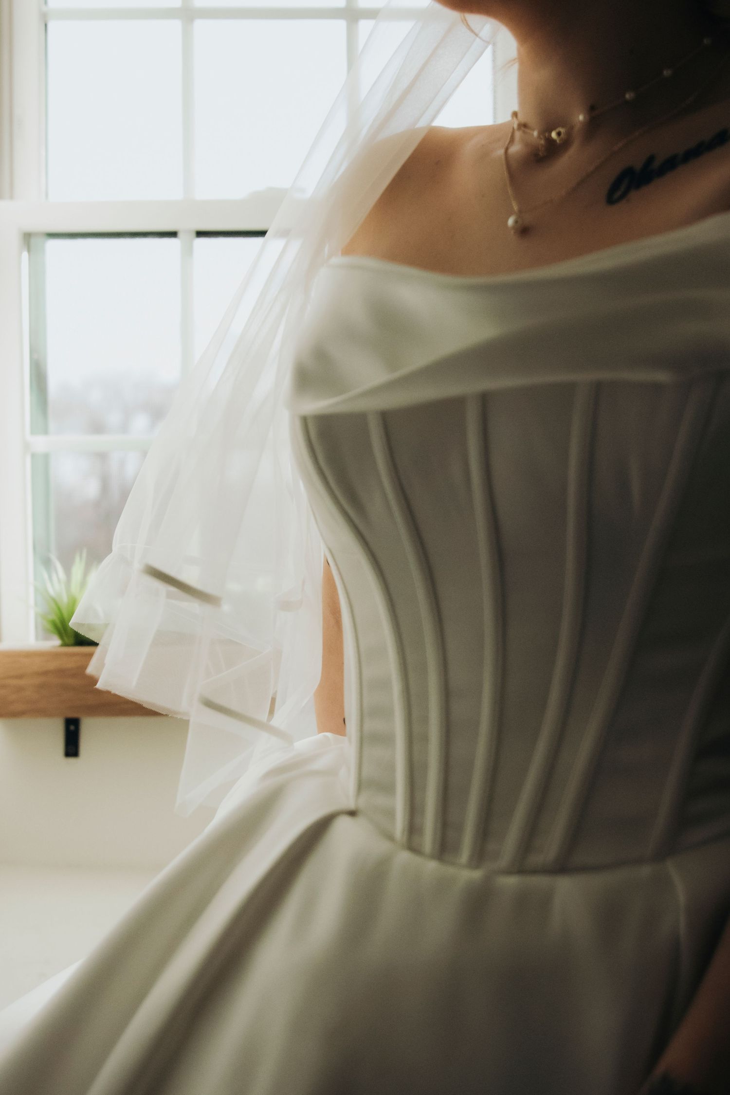 Close-up details of a delicate white wedding dress with soft window light creating an ethereal atmosphere.