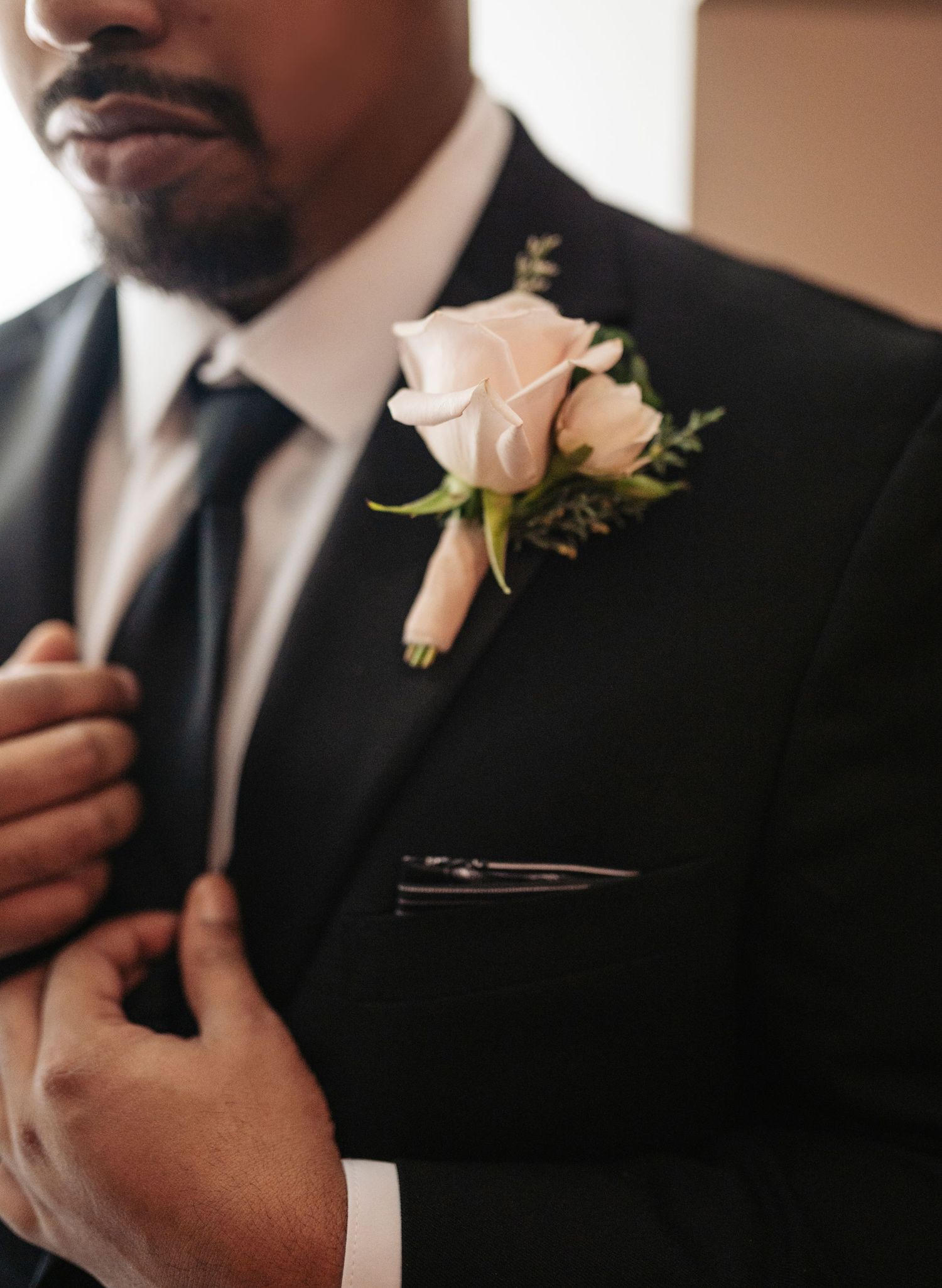 Groom in black tuxedo with blush rose boutonniere pinned to lapel on wedding day.