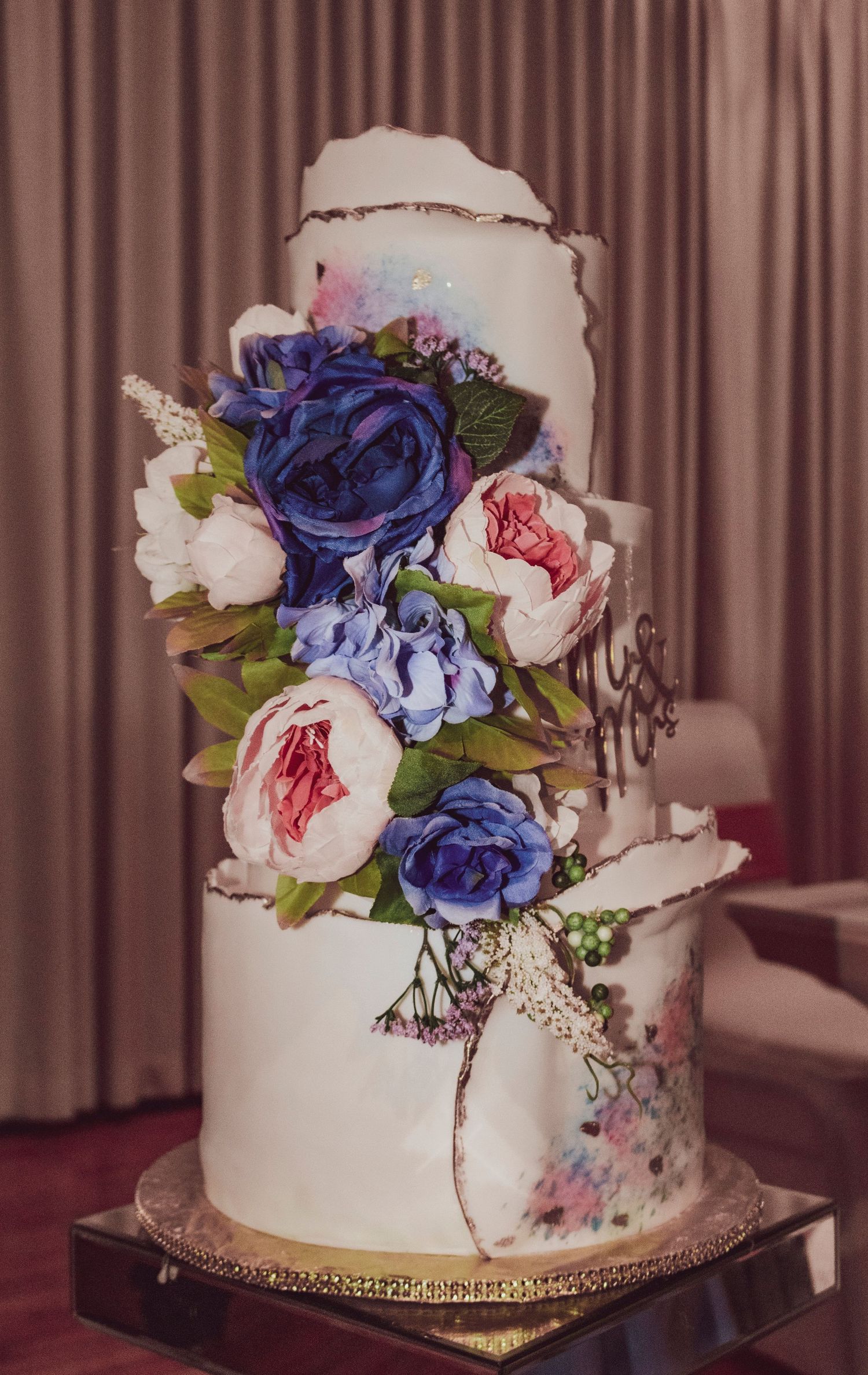 Elegant white wedding cake decorated with blue and pink floral arrangements.