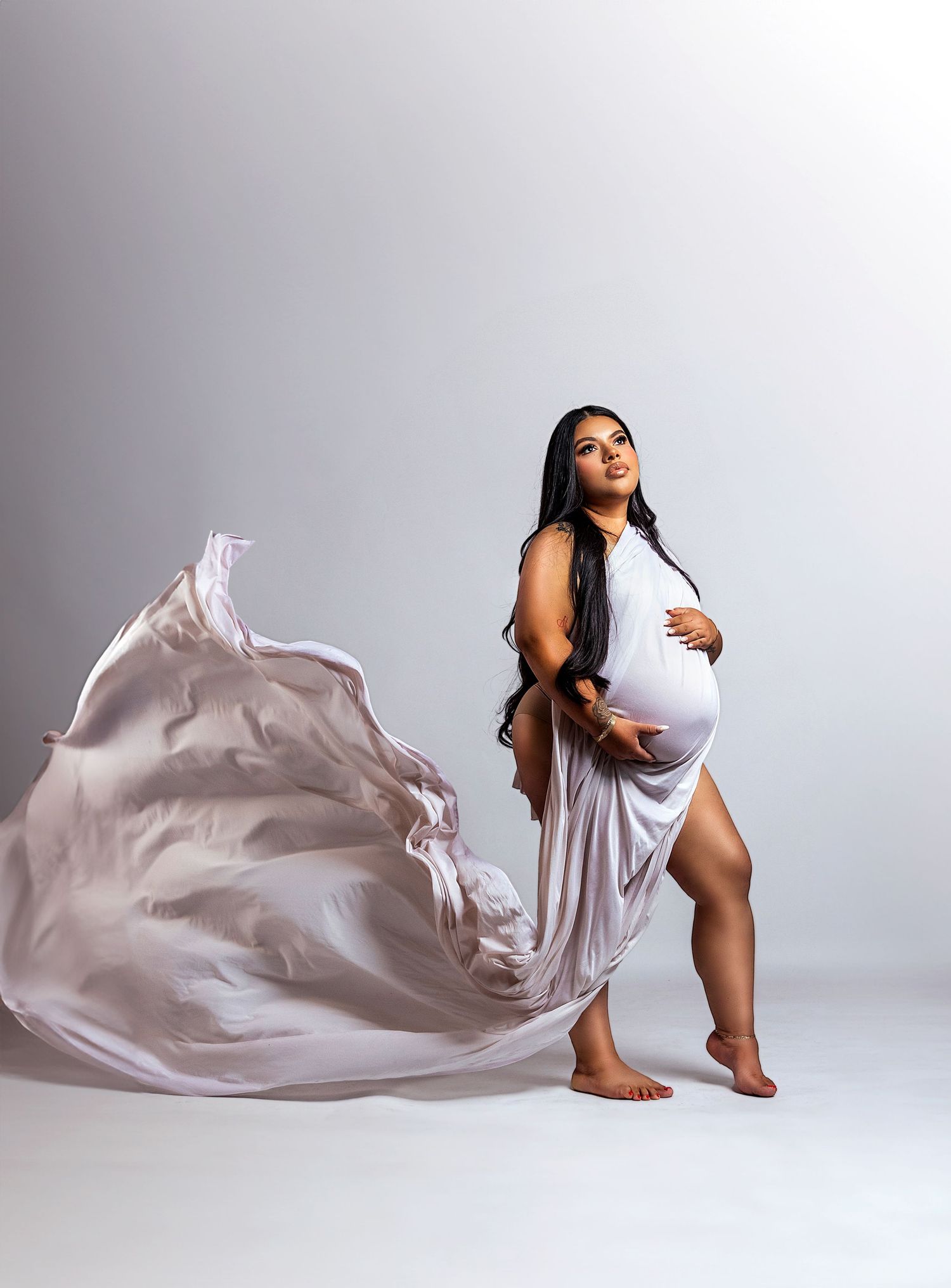 Elegant maternity portrait with flowing fabric against light grey background.