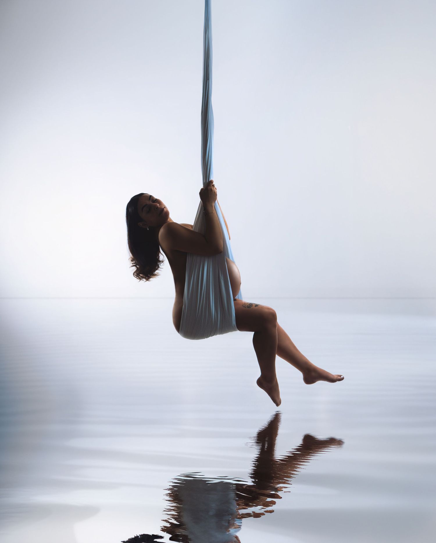 Artistic silhouette of a figure on aerial silk reflected in water with misty atmosphere.