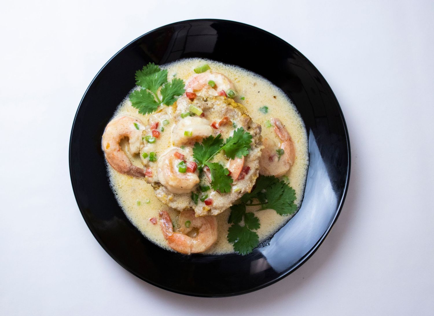 Shrimp in creamy sauce with fresh herbs served on black plate.