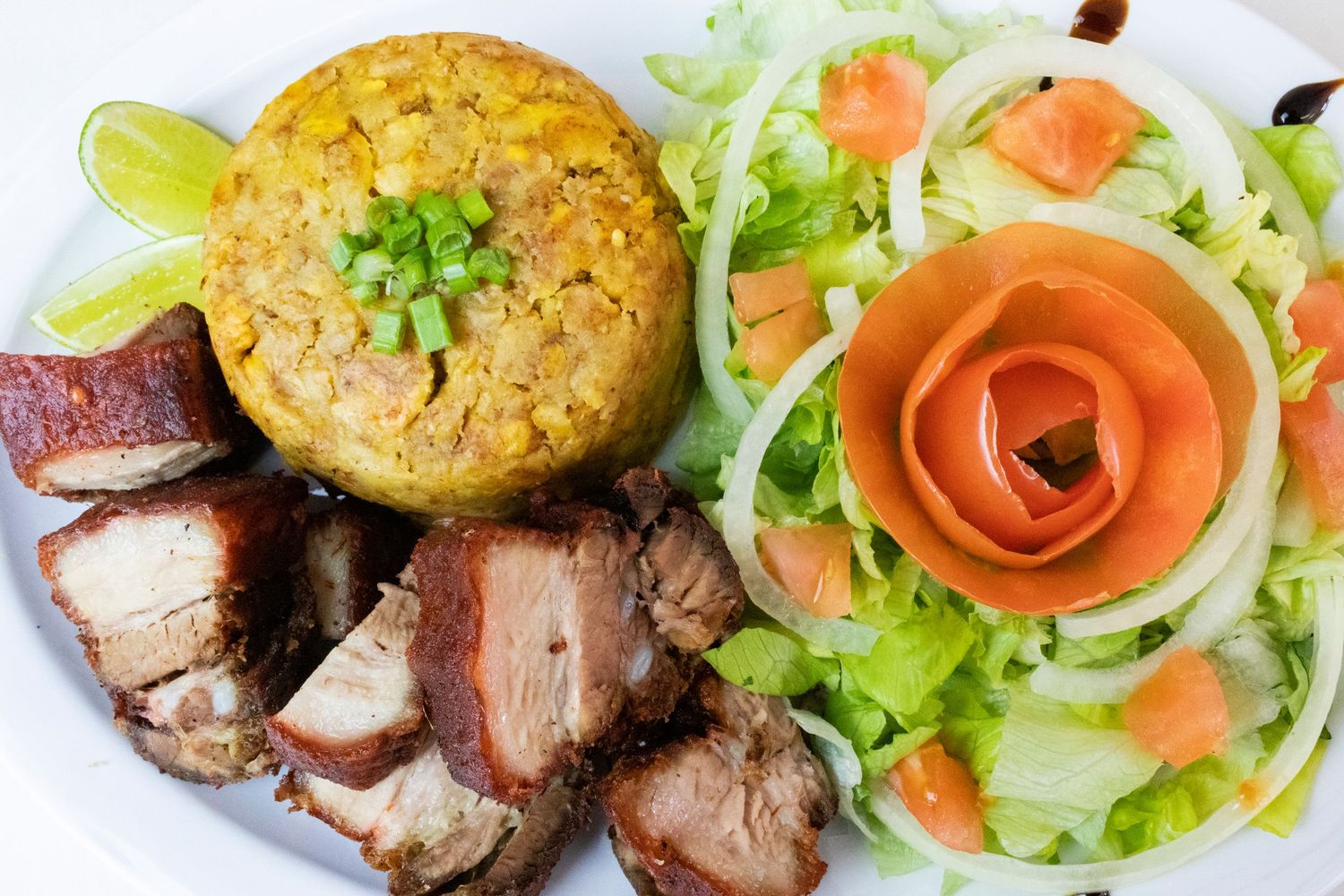 Grilled pork with yellow rice and fresh salad garnished with tomato rose.