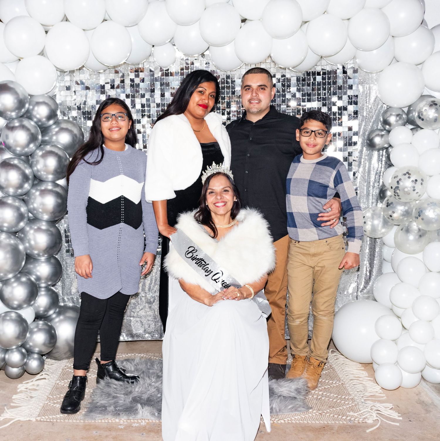 People posing together against a silver balloon wall backdrop decorated for a celebration or party.