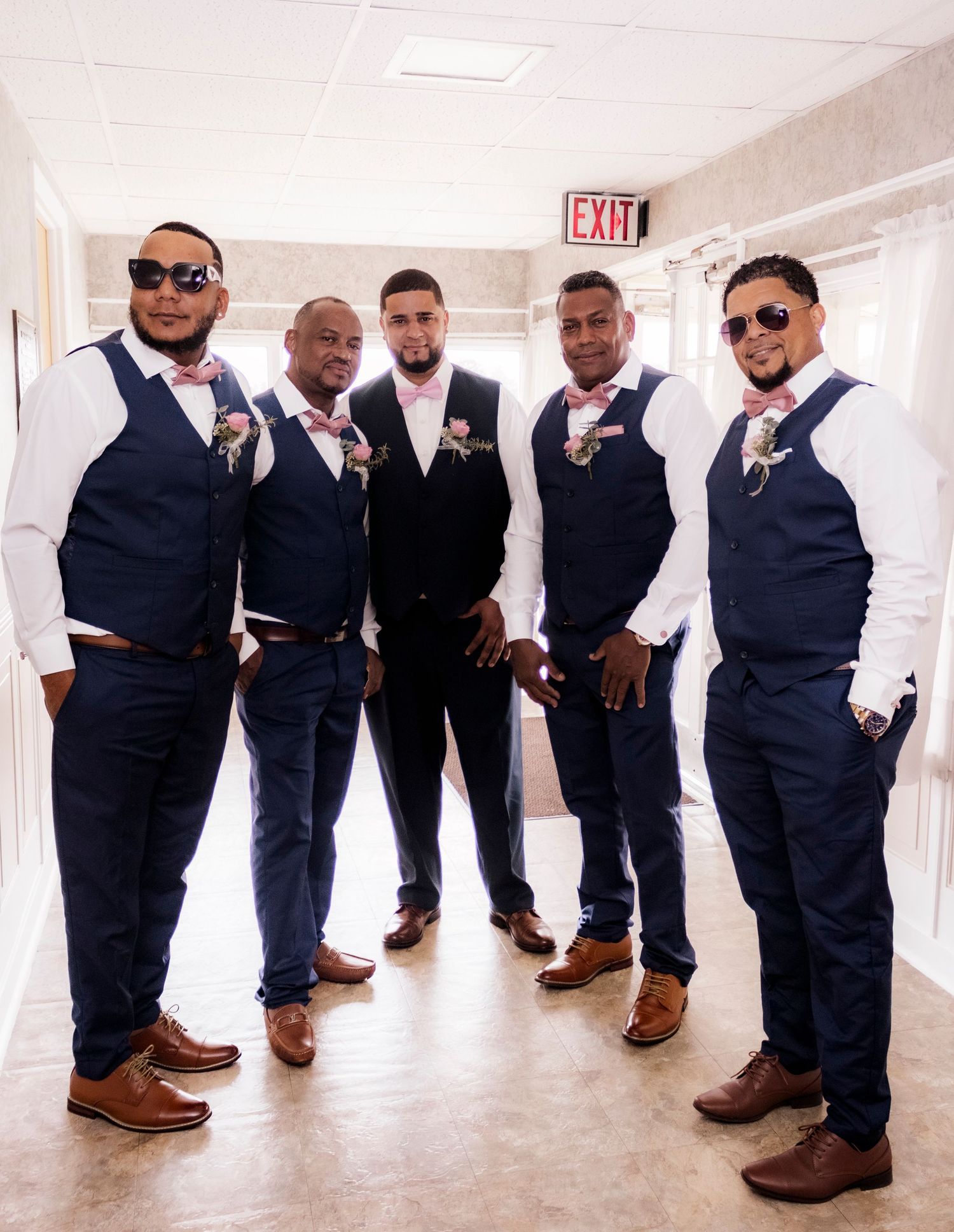 Groomsmen in matching navy vests and bowties pose in hallway.