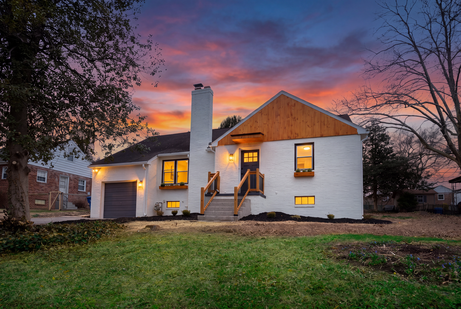 White brick ranch home with attached garage and covered porch glowing at sunset with vibrant orange and purple sky.