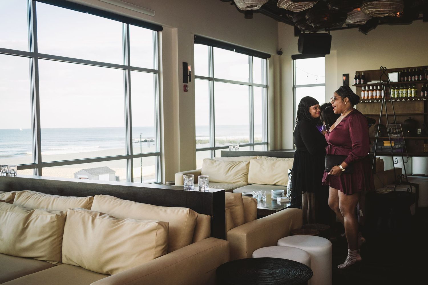 Modern lounge area with white leather couches next to large windows overlooking a waterfront view.