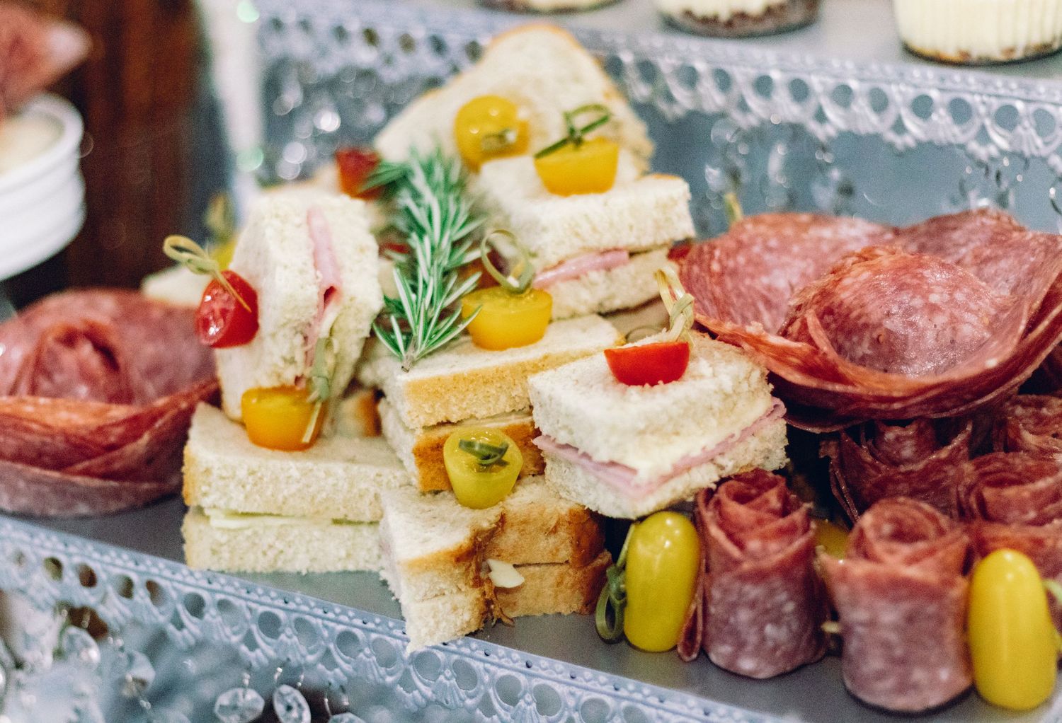 Charcuterie appetizer bites on toasted bread with salami, cheese, pepperoncini and fresh herbs on gray plate.