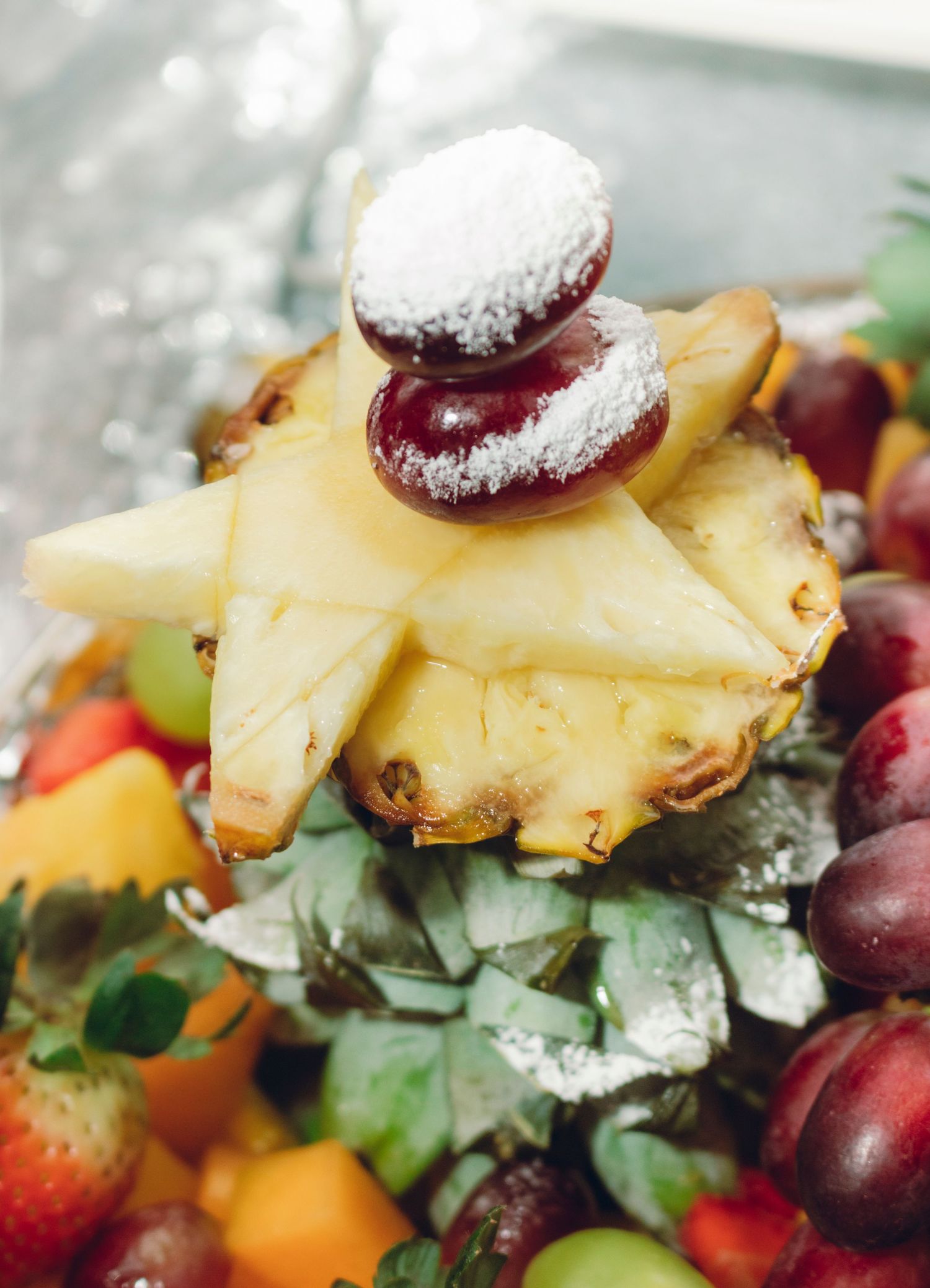 Fresh tropical fruit platter with pineapple slices, berries, grapes and greens arranged in an artful display.
