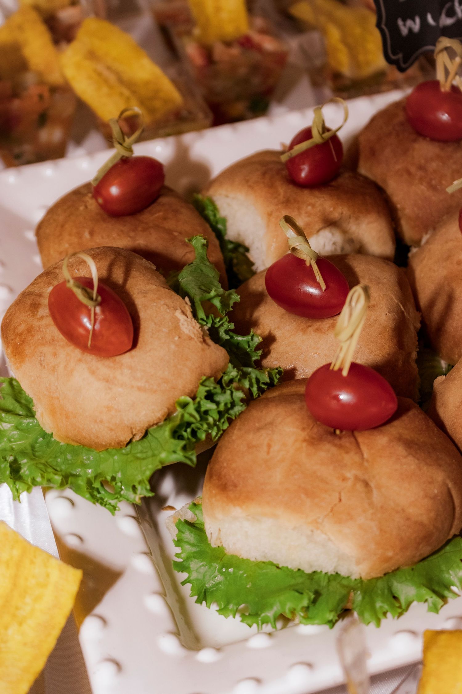 Mini sandwiches garnished with cherry tomatoes and lettuce on a white serving platter.