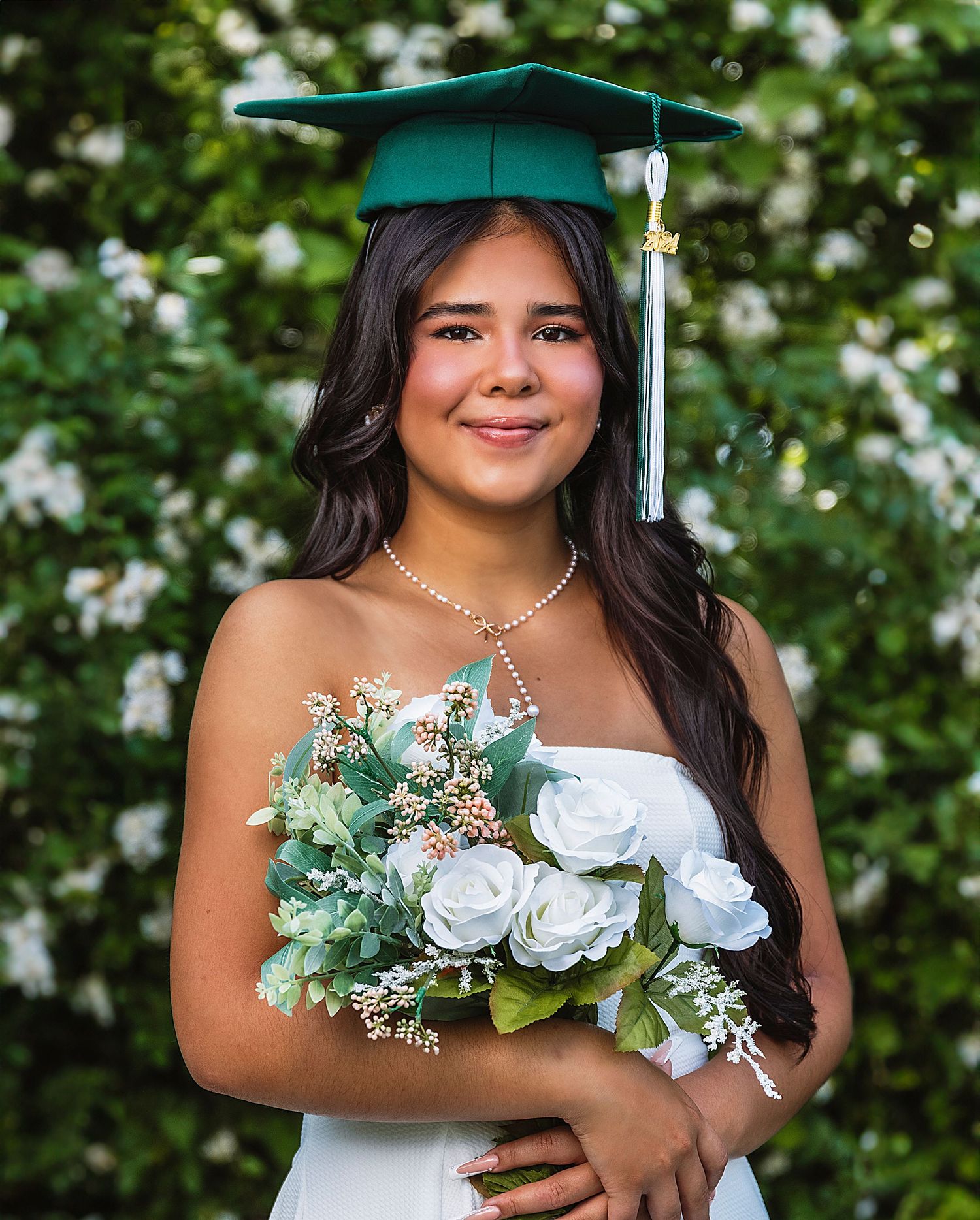 Graduate in teal cap and gown holds white roses during outdoor graduation photoshoot.