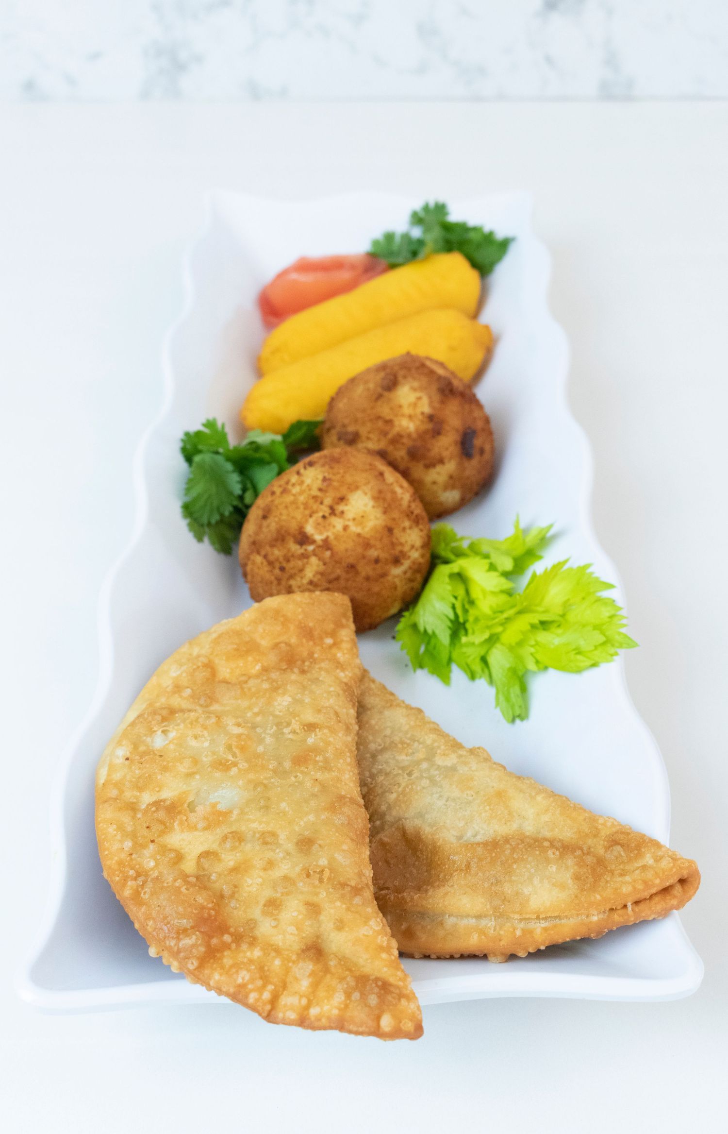 Empanadas and croquettes served with mango slices and fresh herbs on a white plate.