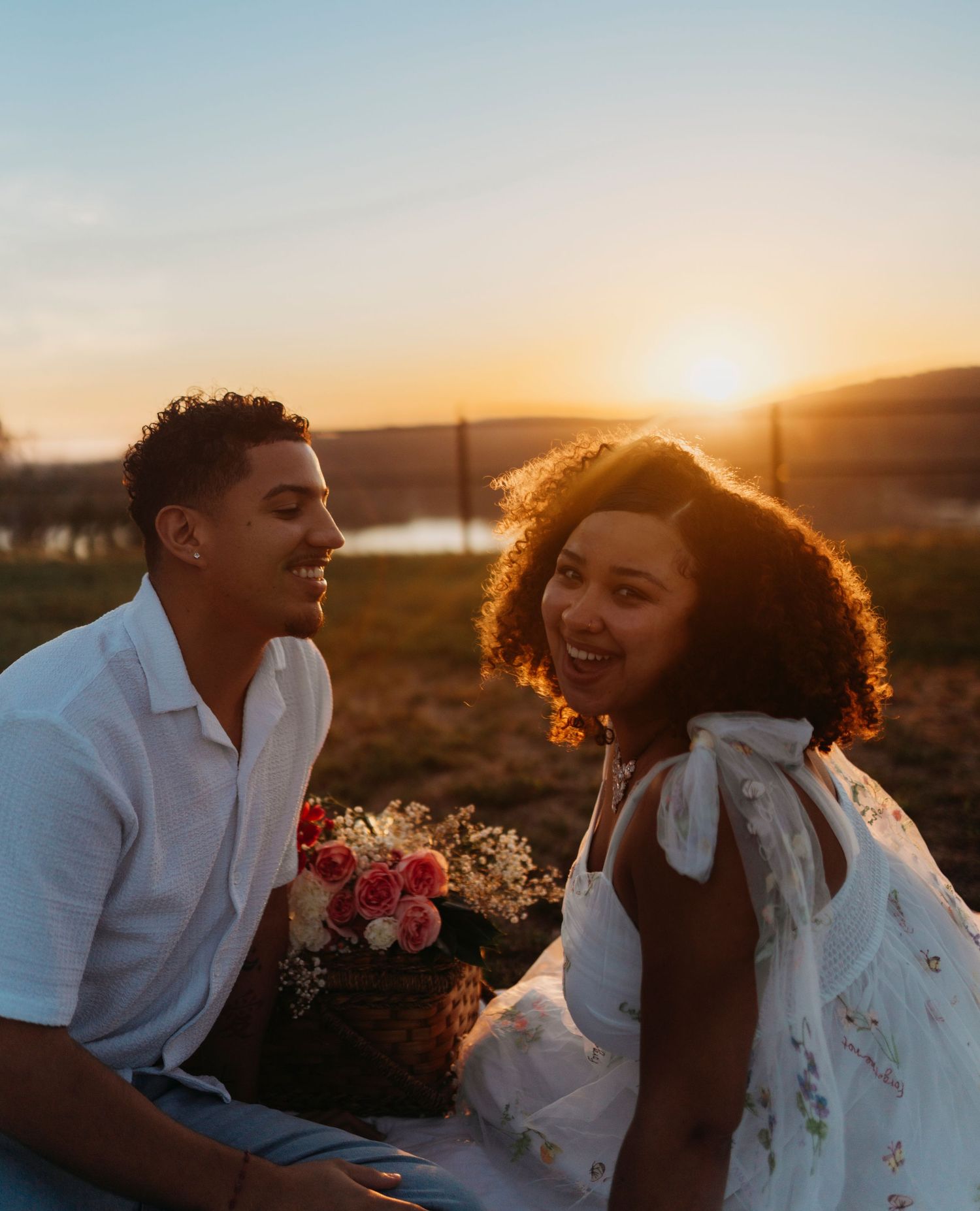 Couple shares intimate moment during golden hour photoshoot in scenic outdoor setting with flowers and mountains.