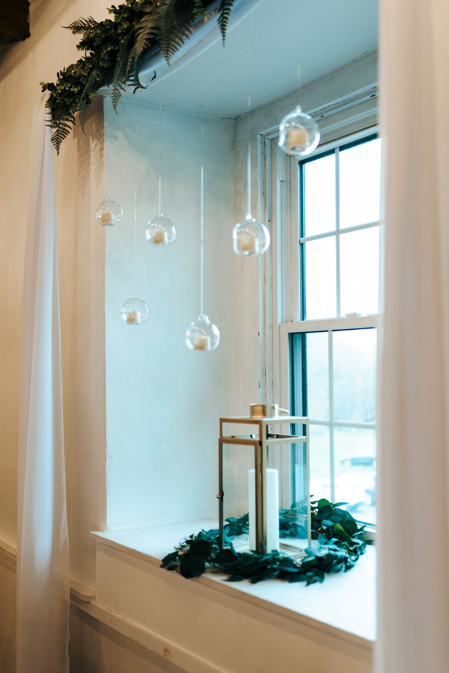 Wedding venue window decorated with hanging glass globe candles and greenery garland.