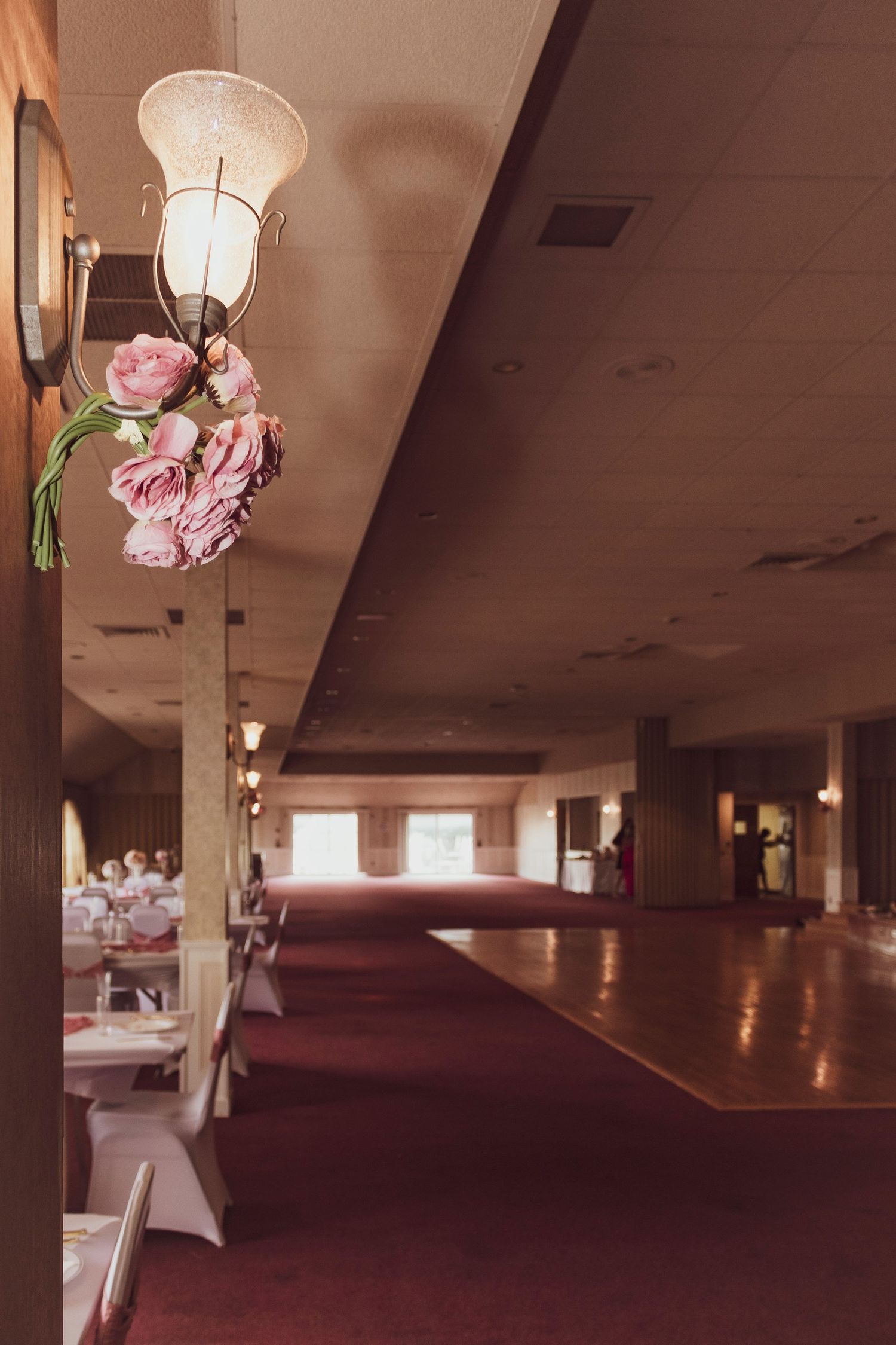 Ballroom venue with pink floral lamp decorations and dark wood dance floor.