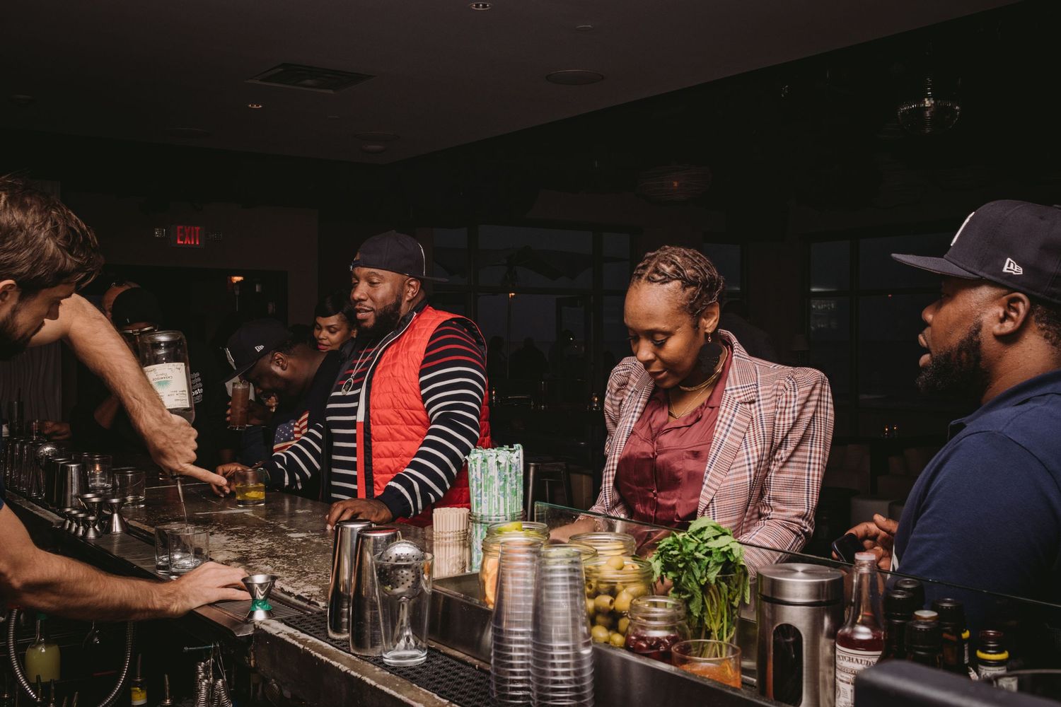 People enjoying drinks and socializing at a dimly lit bar counter with bottles and glasses in view.