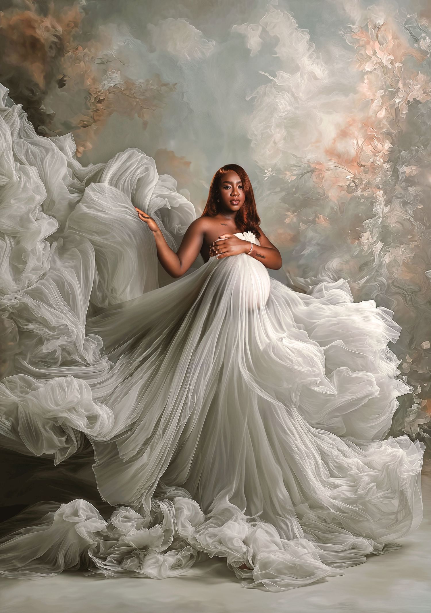 Ethereal maternity portrait with flowing white fabric and dramatic clouds in soft pink and gray tones.