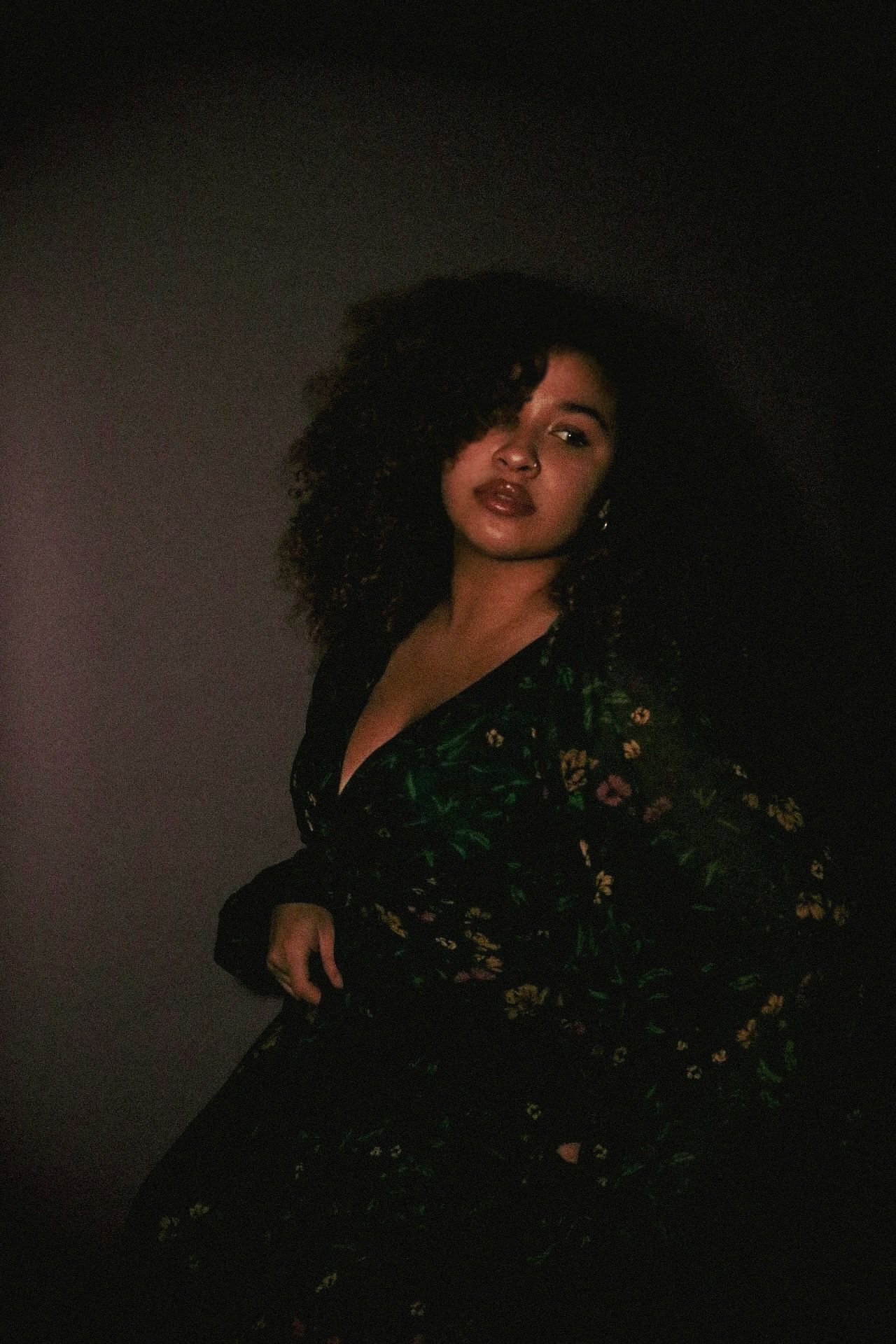 Moody portrait of woman in floral dress against dark background.
