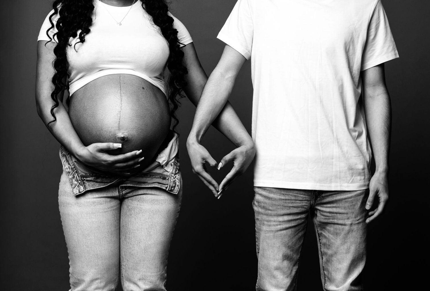 Black and white photo of expecting couple holding hands with focus on pregnant belly.