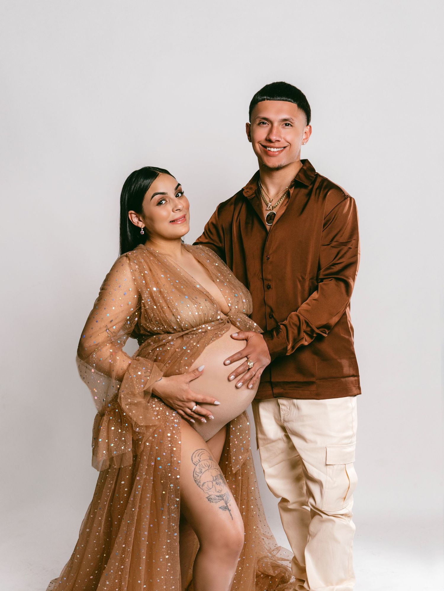 Expecting couple poses together in studio wearing brown and beige formal attire.