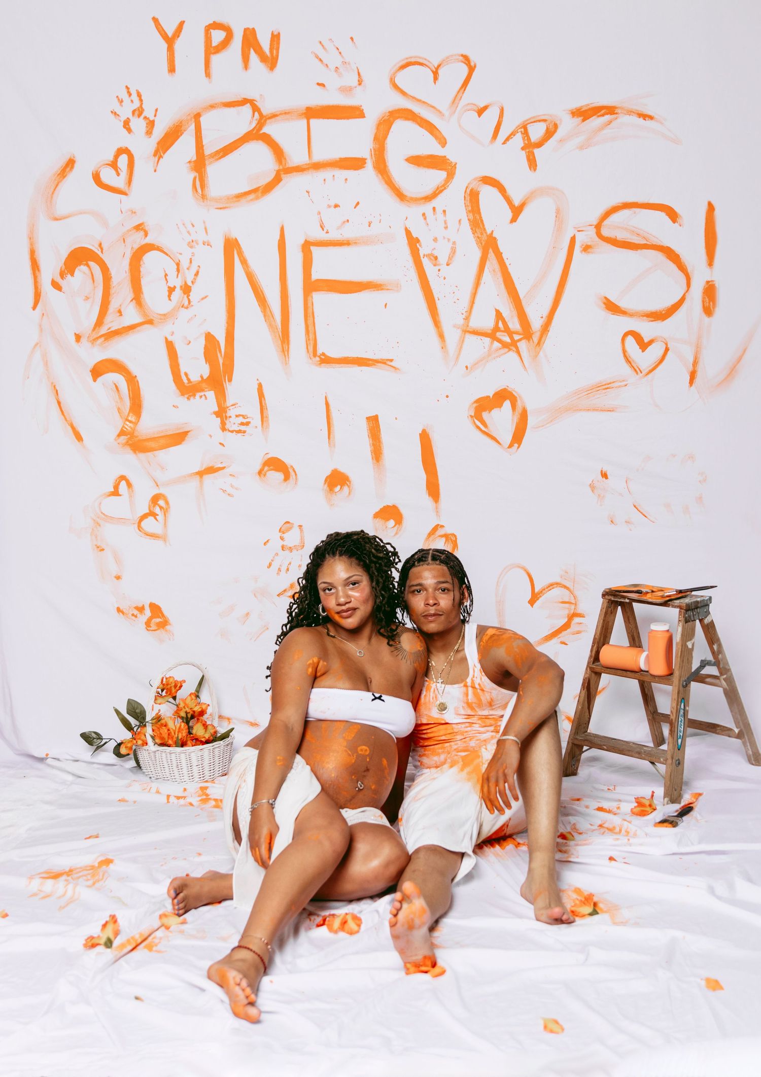 Joyful pregnancy announcement photo with orange paint and handprints on white backdrop.