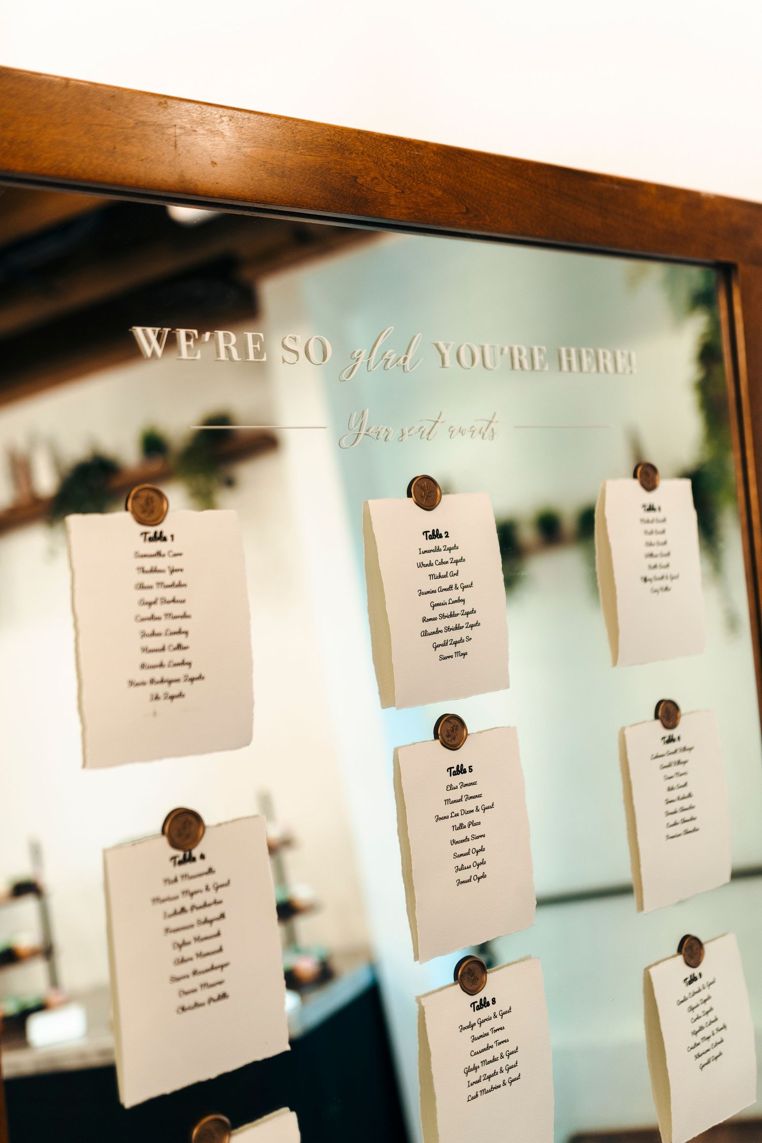 Elegant mirror seating chart display with wax seal table cards reading We're So Glad You're Here.