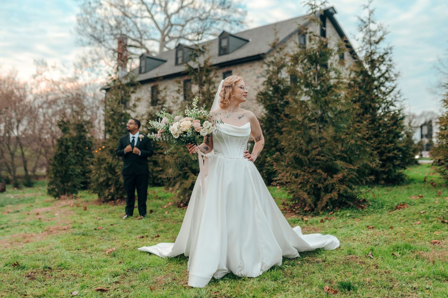 Bride in elegant white ball gown holding bouquet with groom standing in background.