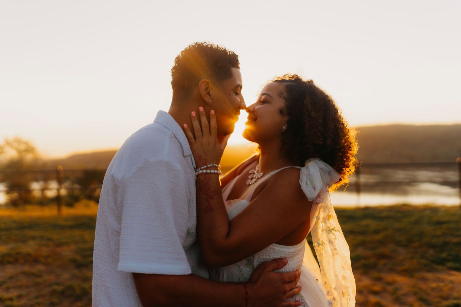 Romantic couple embraces during golden hour sunset in a scenic outdoor setting.